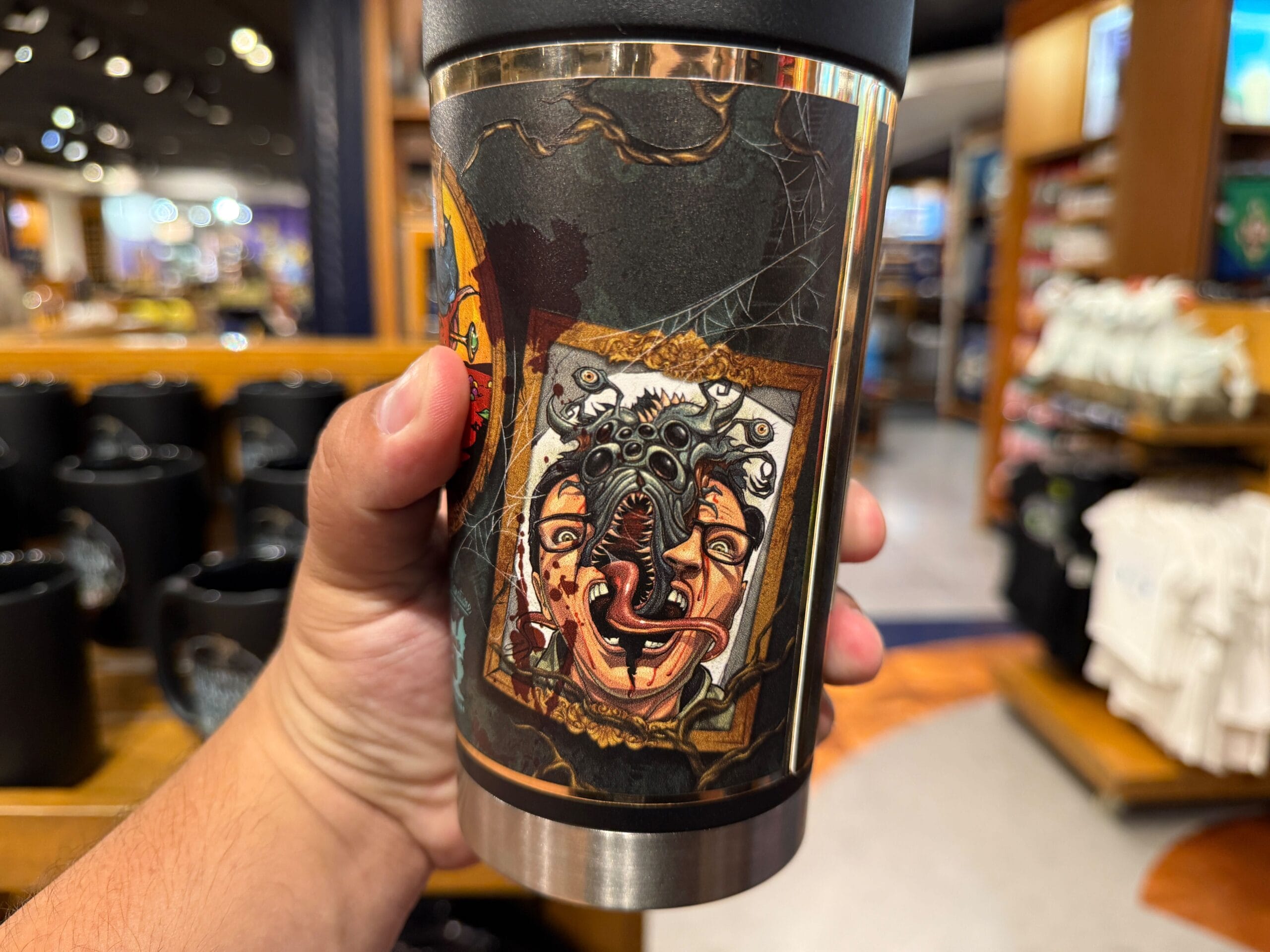 A hand holds a travel mug with a surreal, monstrous face—perfect HHN Merch 2025 at Universal Orlando Resort.