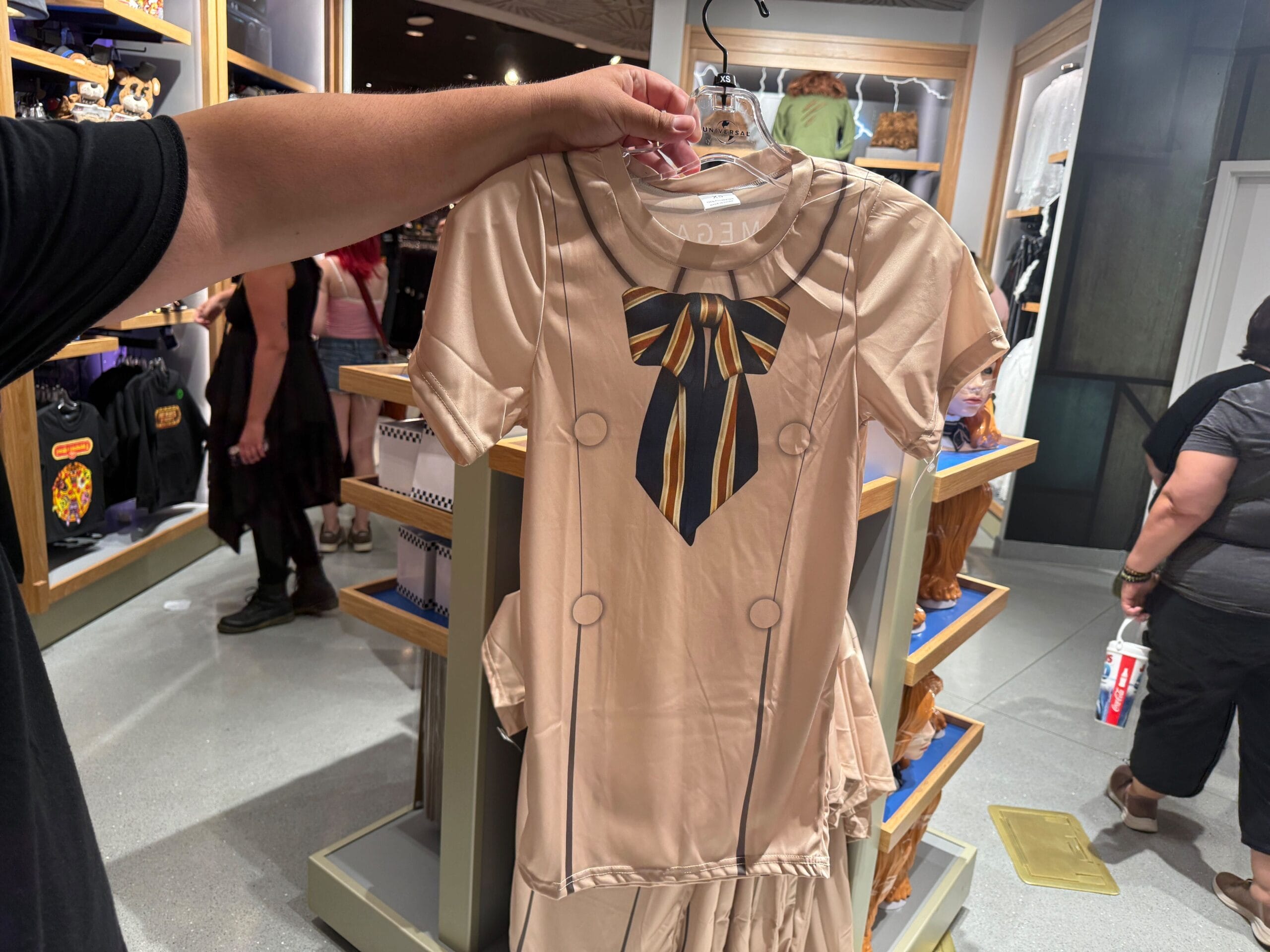 A person holds up a beige dress with a printed bowtie design at Universal Orlando Resort.
