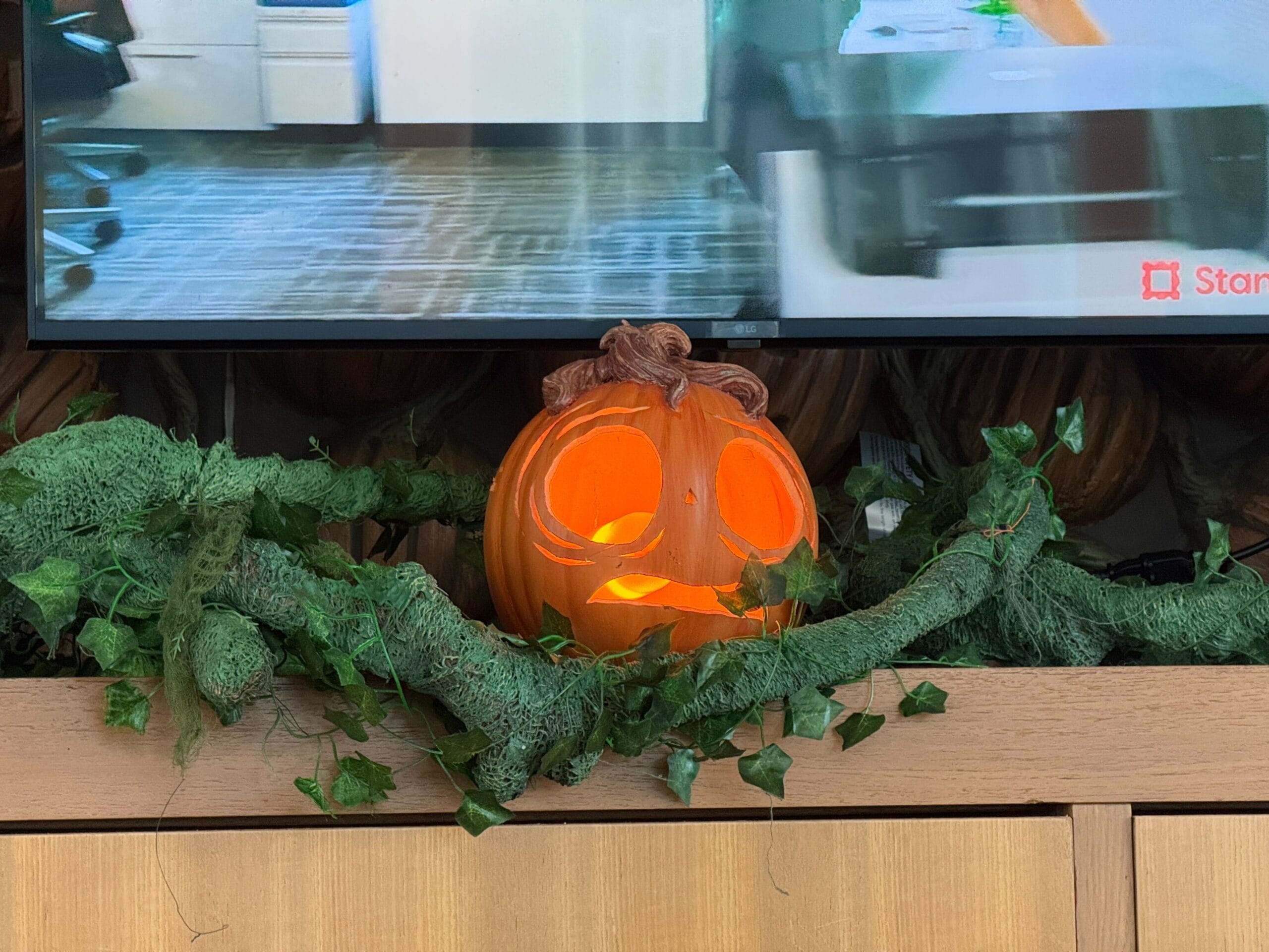 A glowing jack-o’-lantern with curly hair sits among fake vines beneath a TV at Cabana Bay Beach Resort.