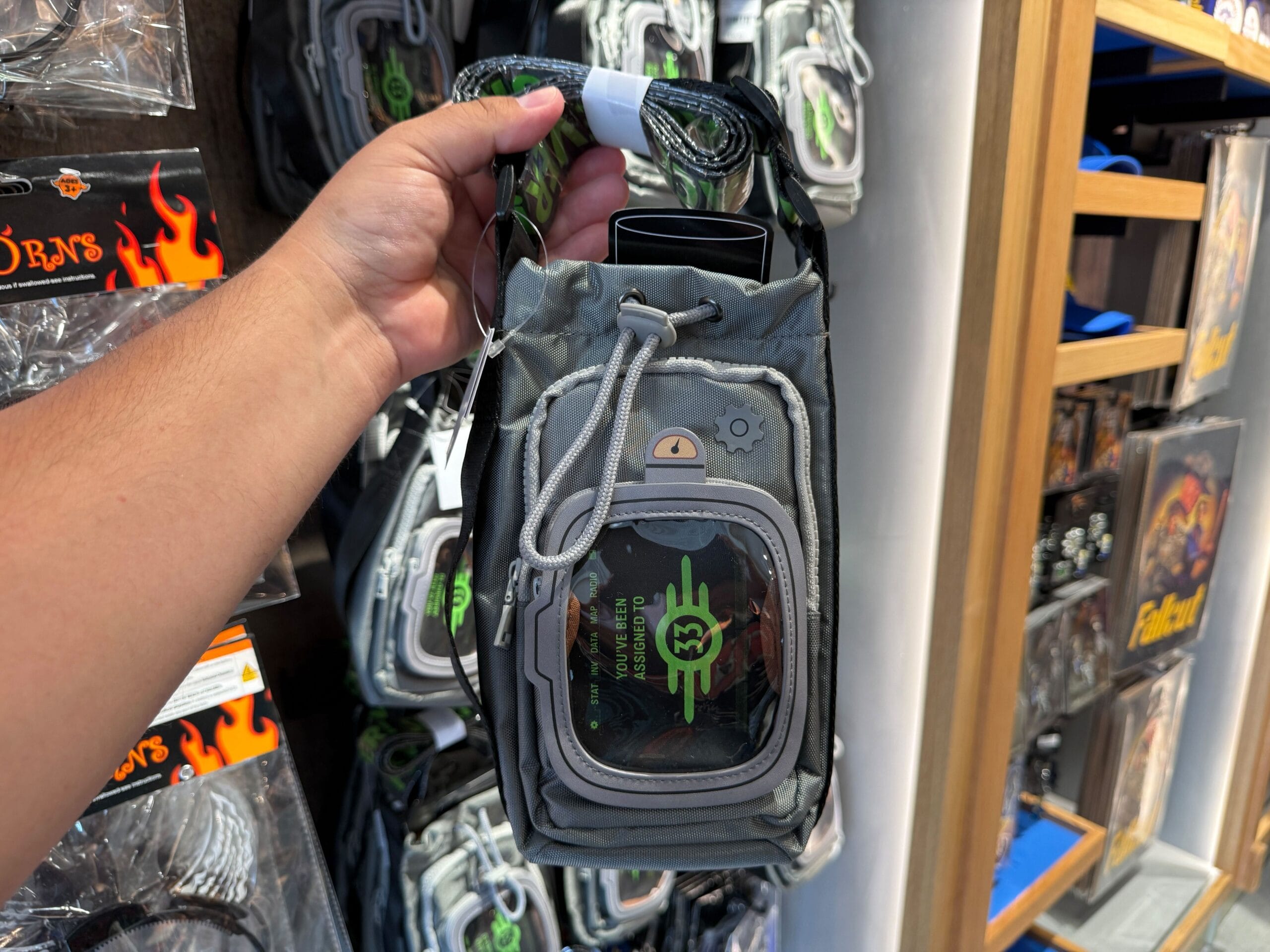 A hand holds a small gray Monster Energy-themed bag, exclusive HHN merch at Universal Orlando Resort's display.