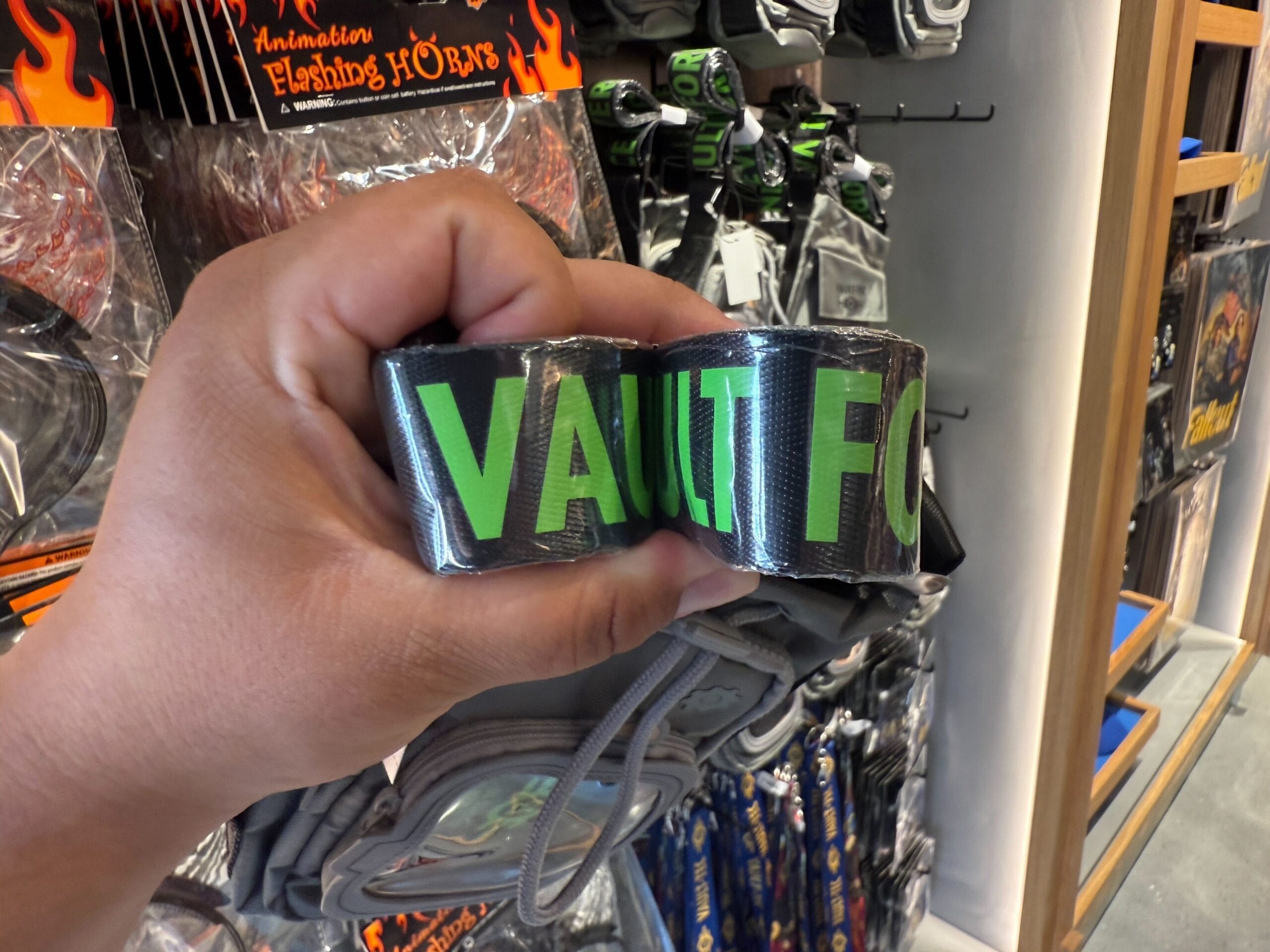 A hand holds a shiny black belt with bold green "VAULT" text—perfect HHN merch for Halloween Horror Nights 2025 collectors.