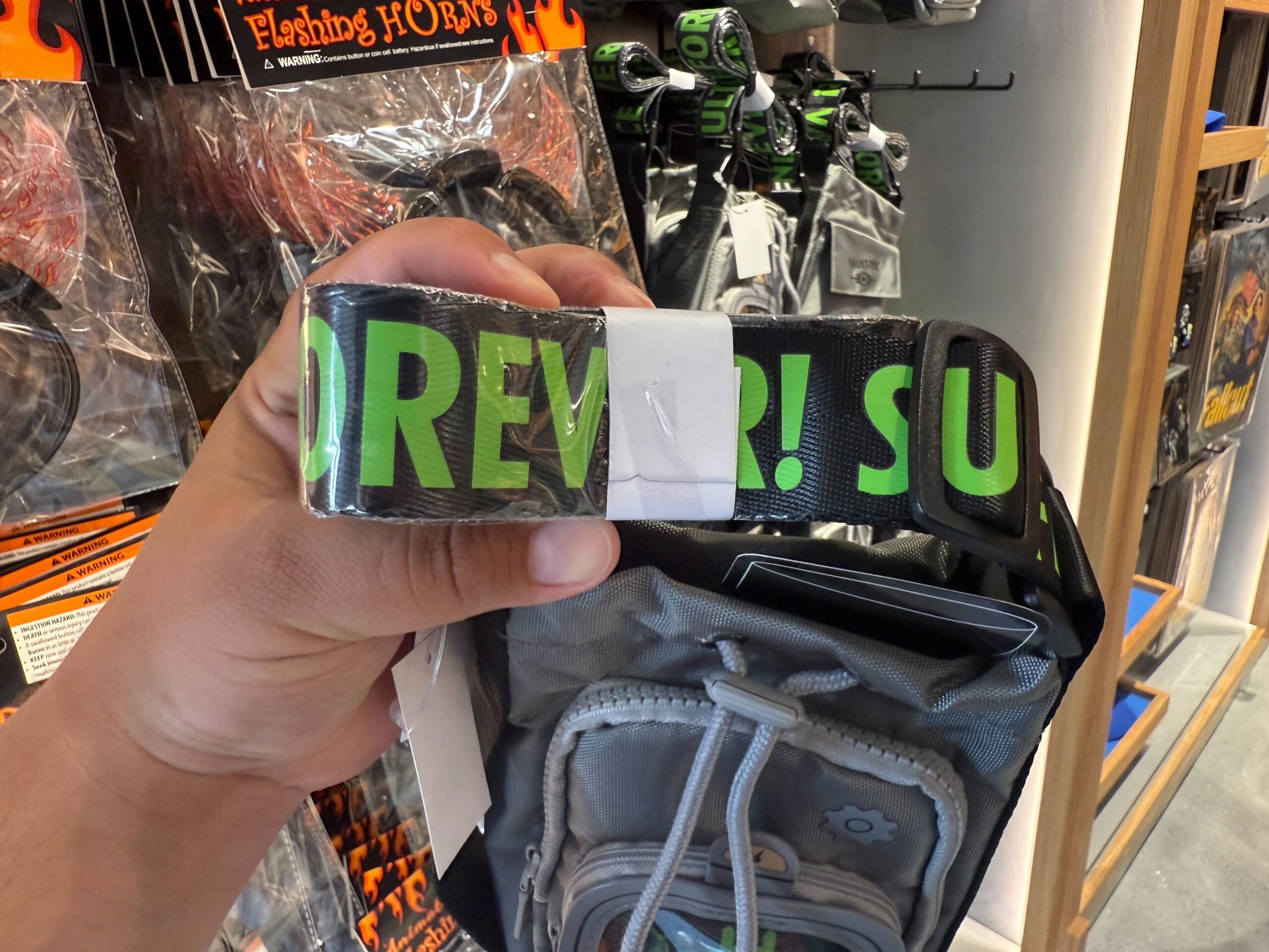 A hand holds a black strap with bright green "FOREVER! SUM" letters, part of new HHN merch at Universal Orlando Resort.