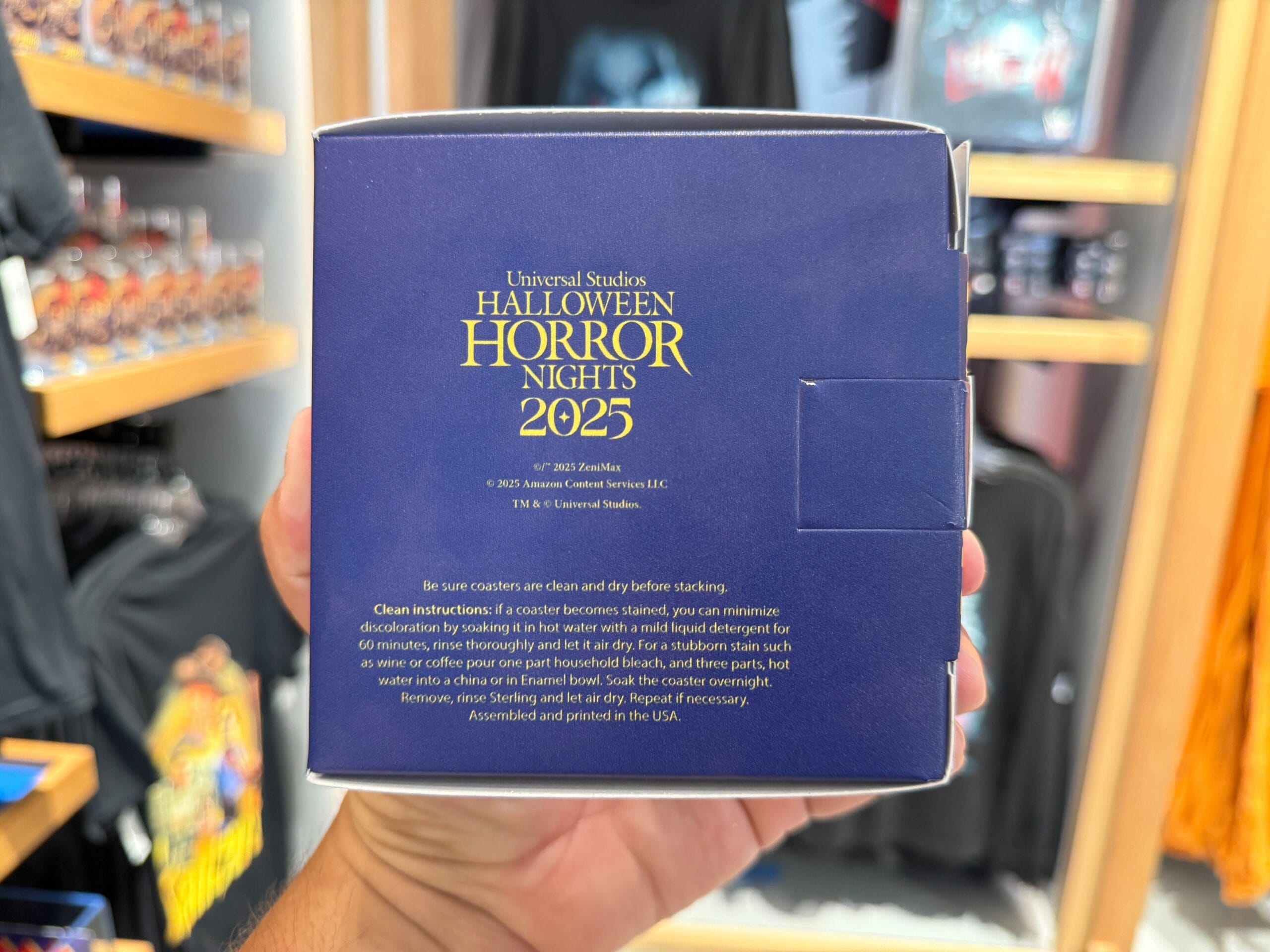 A hand holds a blue HHN merch box with gold text and coaster care instructions at Universal Orlando Resort.