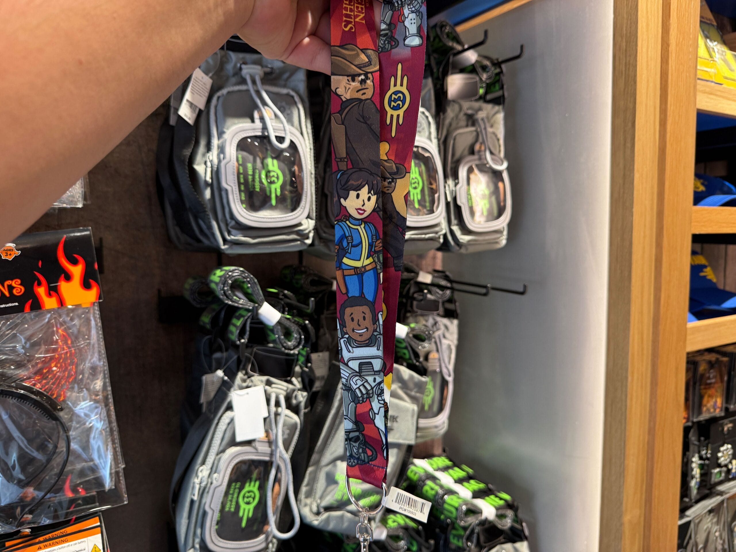 A hand holds a "Stranger Things" lanyard in front of HHN Merch on display at Universal Orlando Resort.