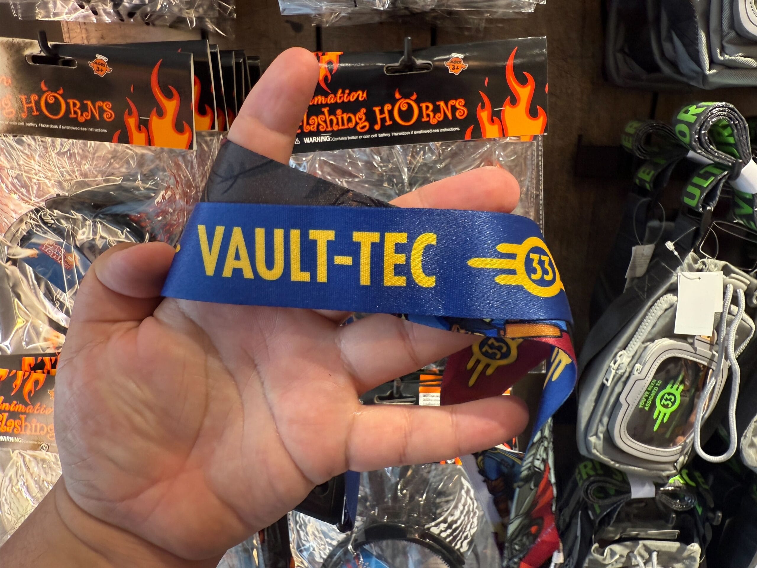 A hand holds a blue lanyard with "VAULT-TEC 33," part of HHN merch at Universal Orlando Resort.