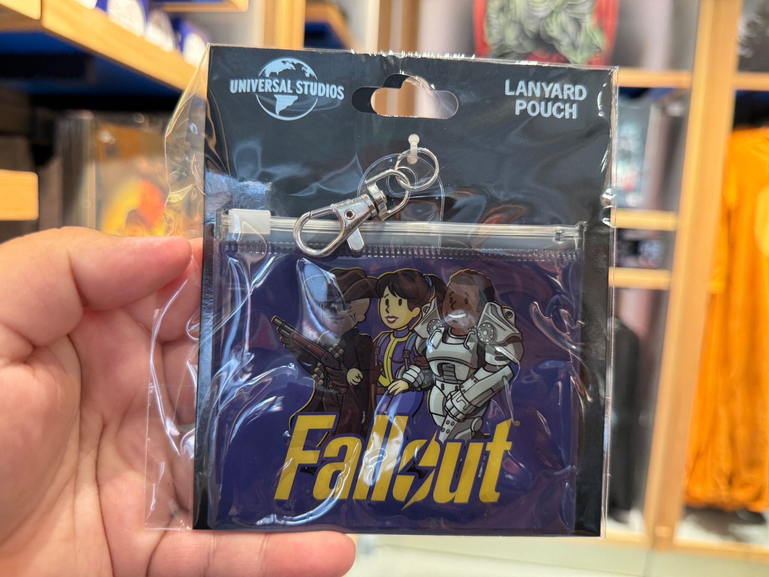 Hand holding a packaged Fallout lanyard pouch from HHN Merch at Universal Orlando Resort, featuring cartoon characters and logo.