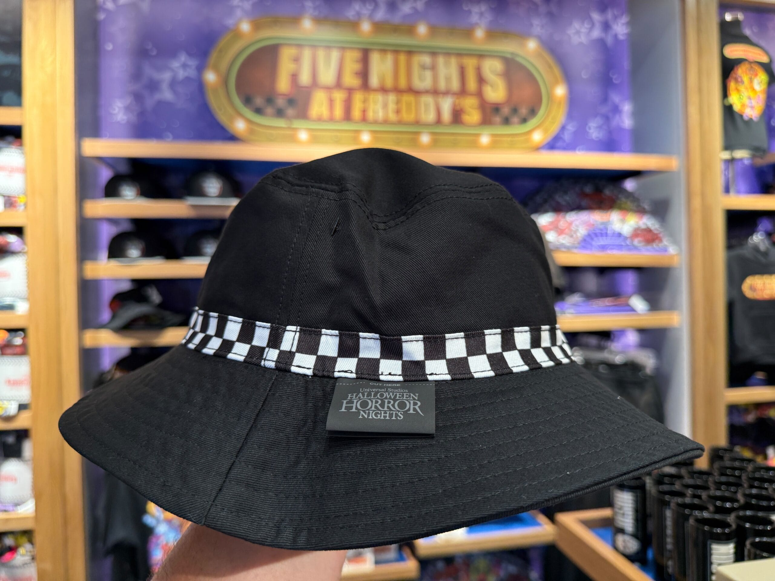A black bucket hat with a checkered band and "Halloween Horror Nights" label, held at Universal Orlando Resort.