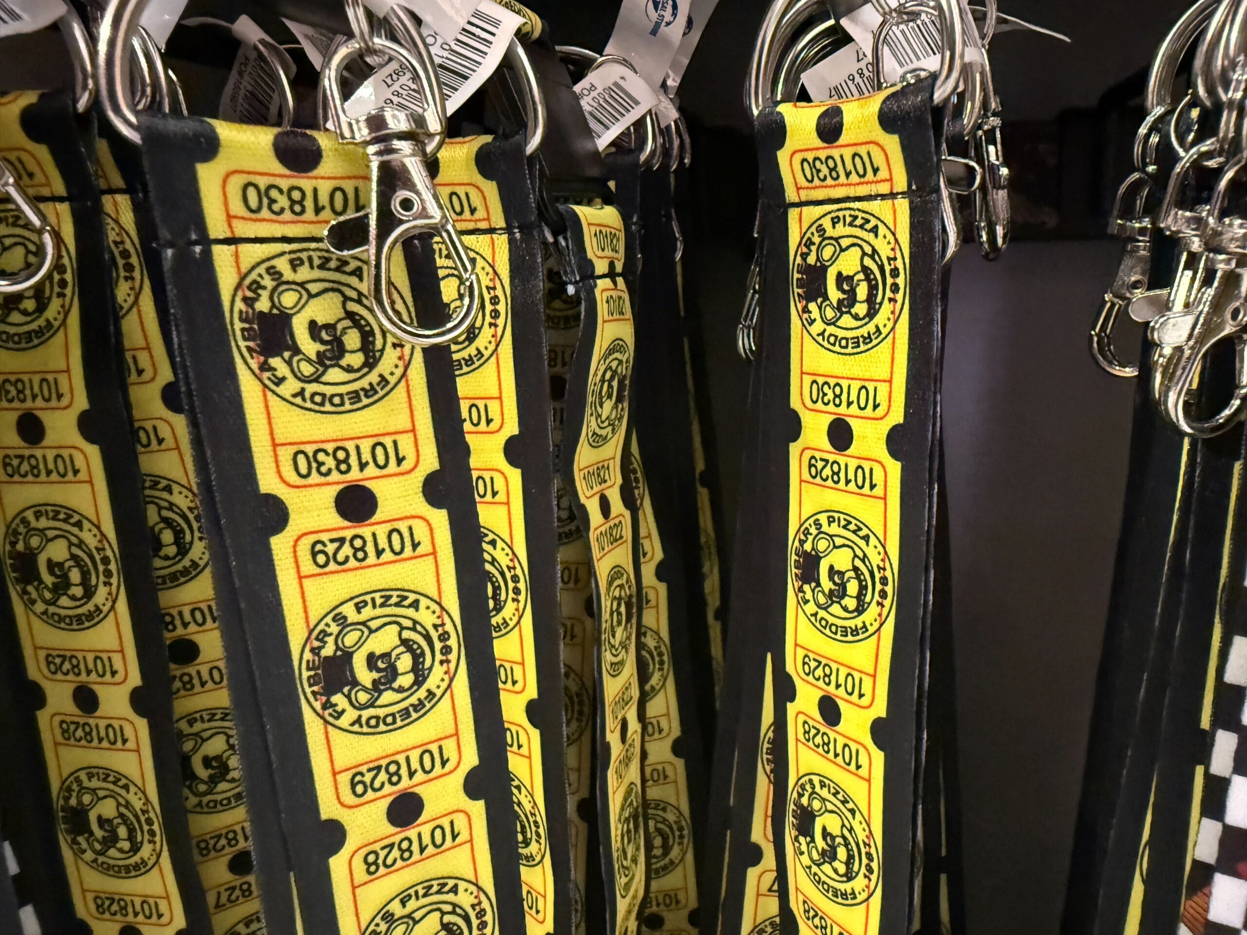 Yellow lanyards with black text and logos for Pedro’s Pizza, inspired by Universal Orlando Resort HHN merch, hang on display hooks.