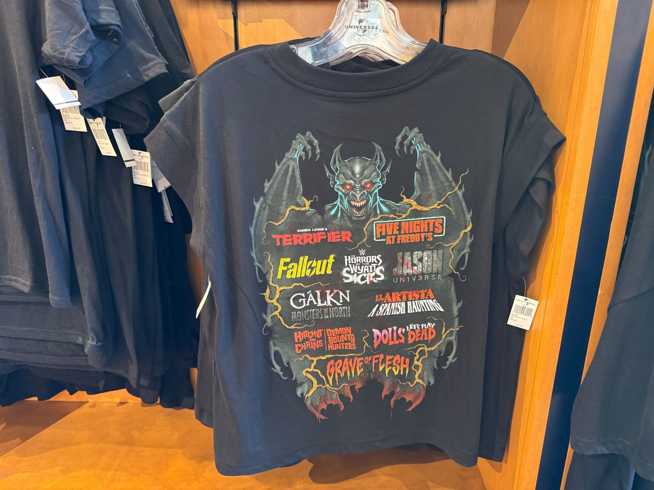 Black t-shirt with a red demon graphic and colorful horror titles, perfect for HHN Merch at Universal Orlando Resort.