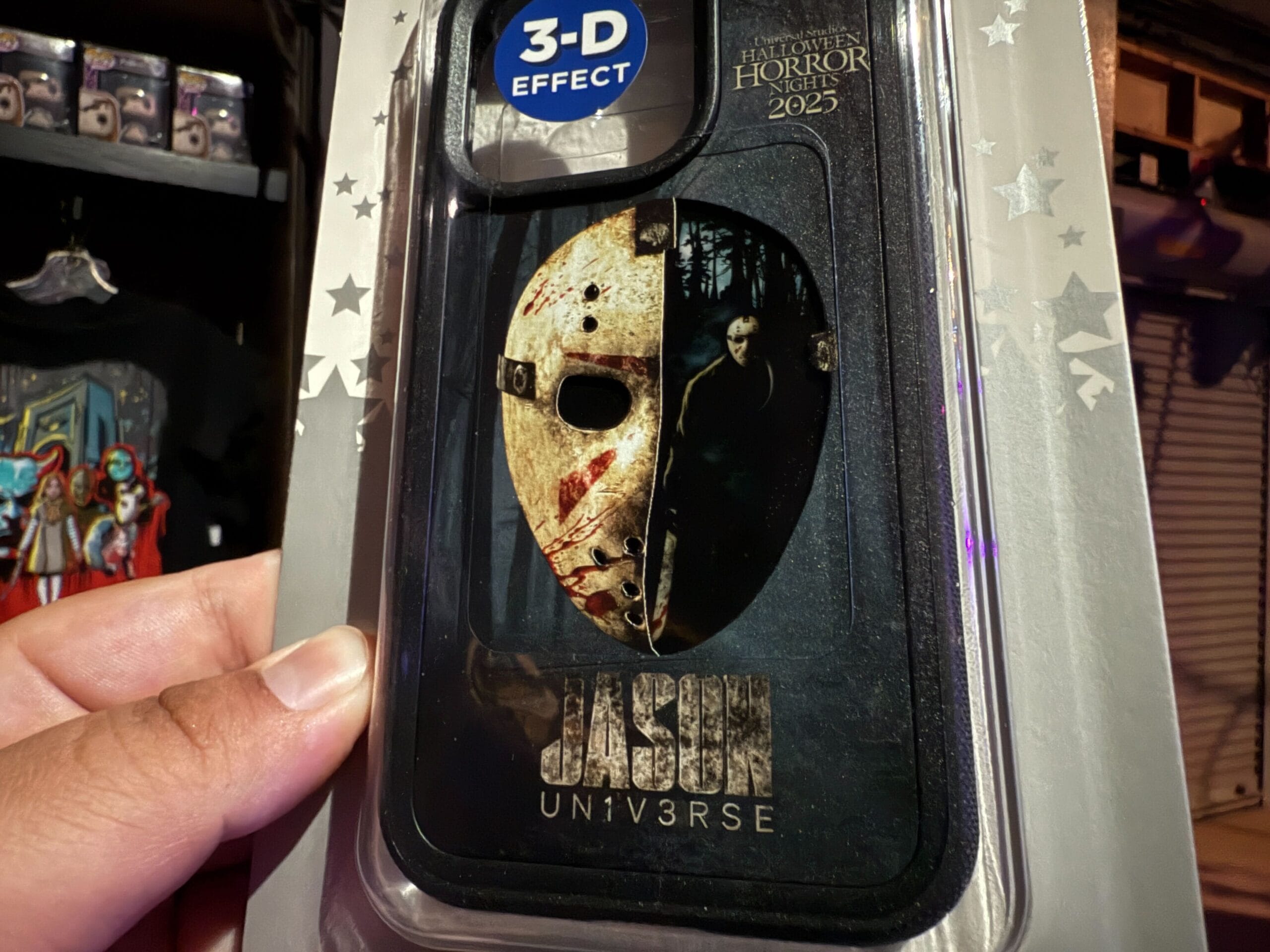 A hand holds a phone case with Jason's mask and "Halloween Horror Nights 2025" at Universal Orlando Resort.
