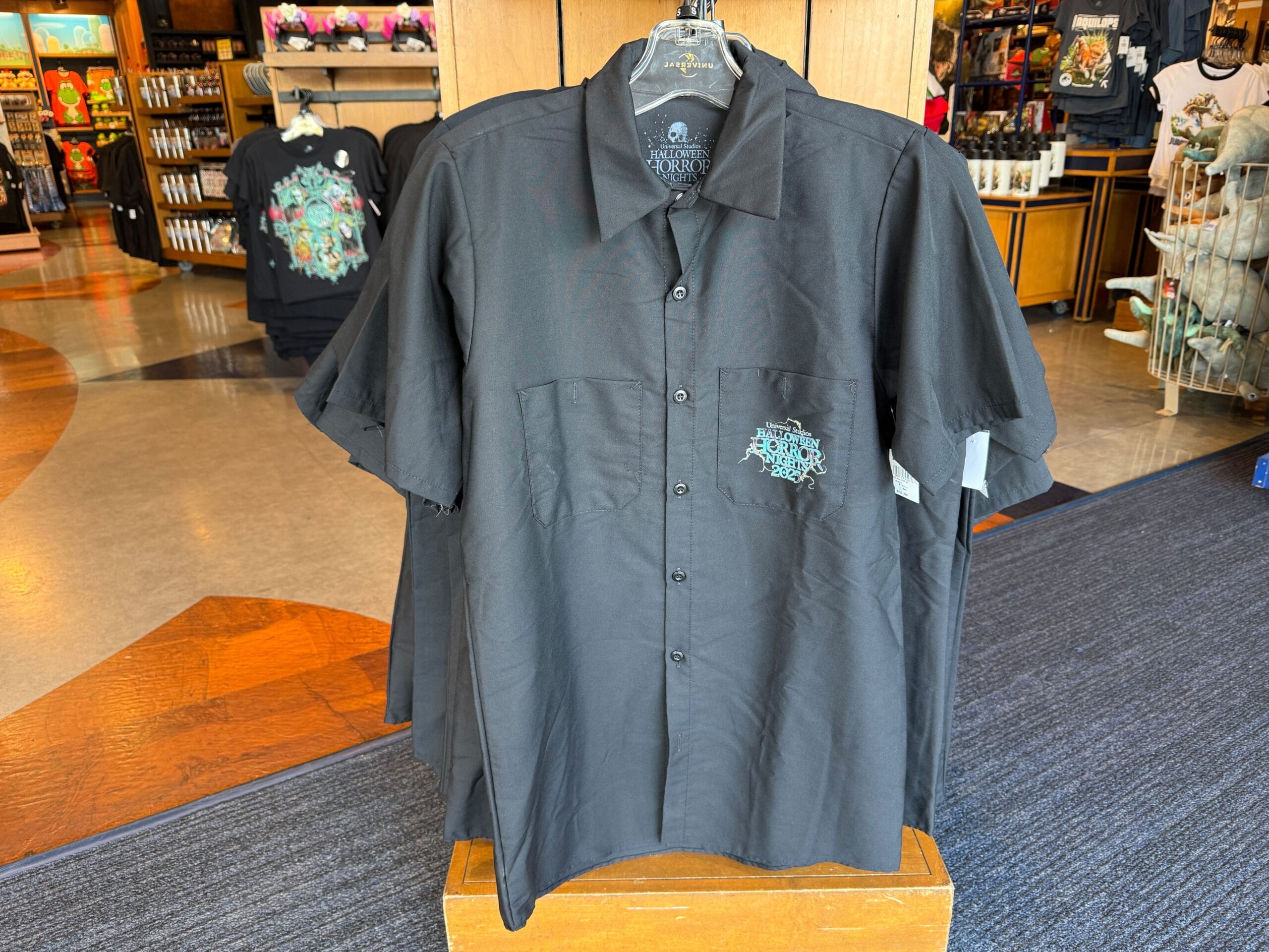 A black button-up shirt with a small embroidered Haunted Mansion logo, featured as HHN merch in a Universal Orlando Resort store.