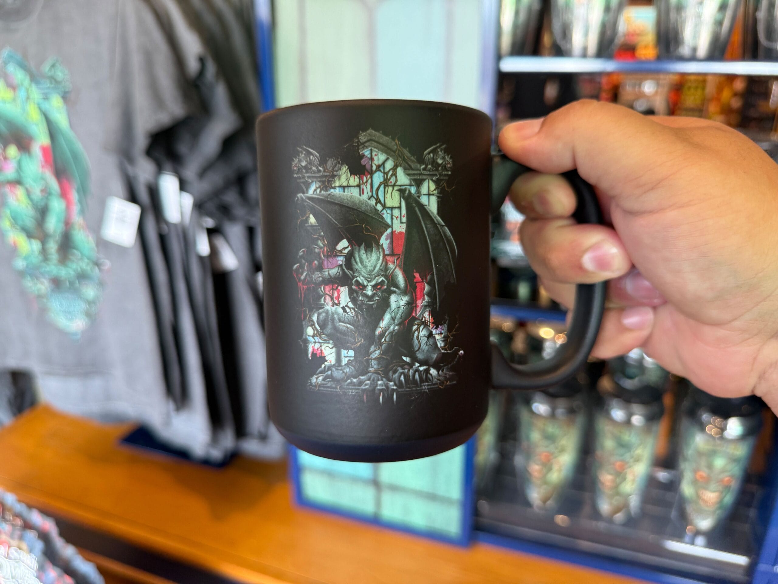 A hand holds a black HHN Merch mug with a gothic dragon and stained glass, at Universal Orlando Resort.