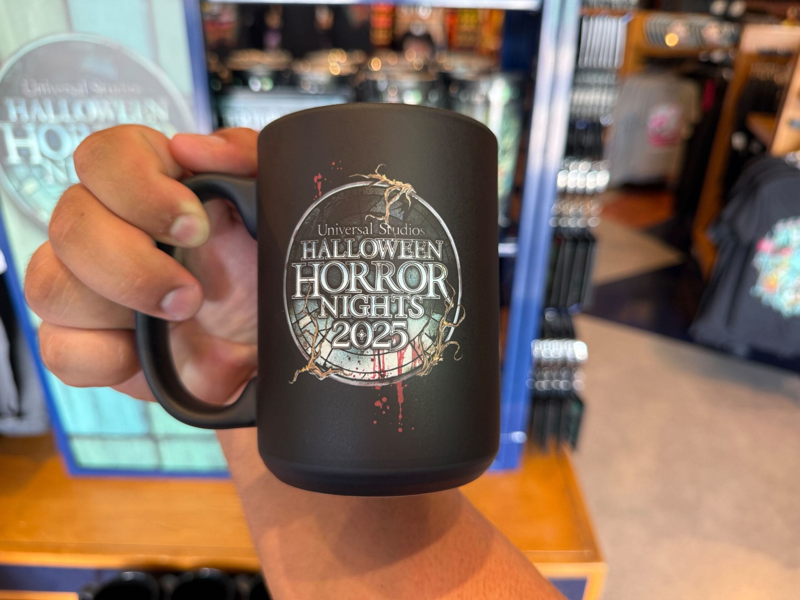 Hand holding a black HHN merch mug with “Universal Studios Halloween Horror Nights 2025” logo at Universal Orlando Resort.