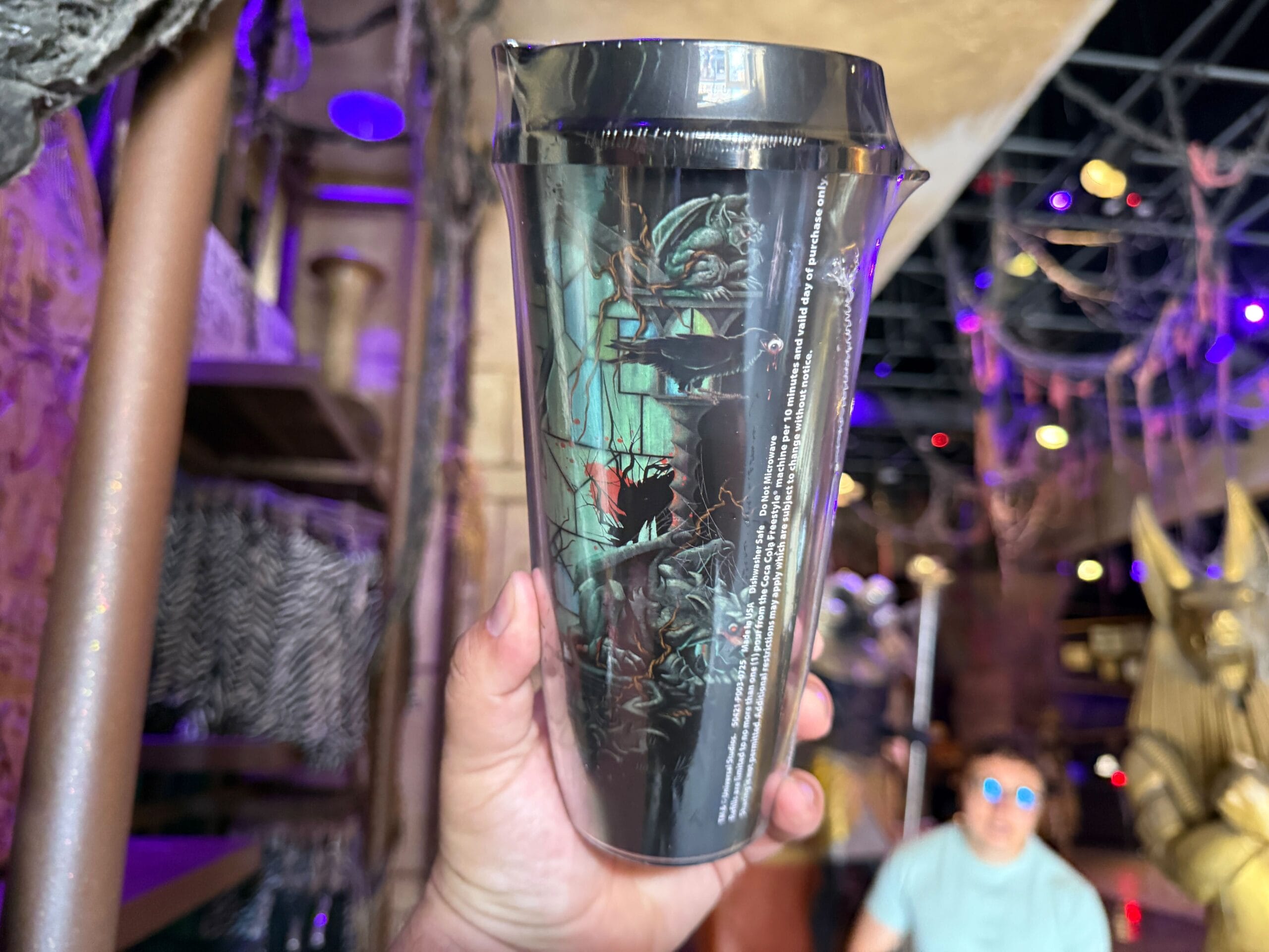 A hand holds a shiny black cup with Maleficent as a dragon, perfect for Halloween merchandise in a themed store.