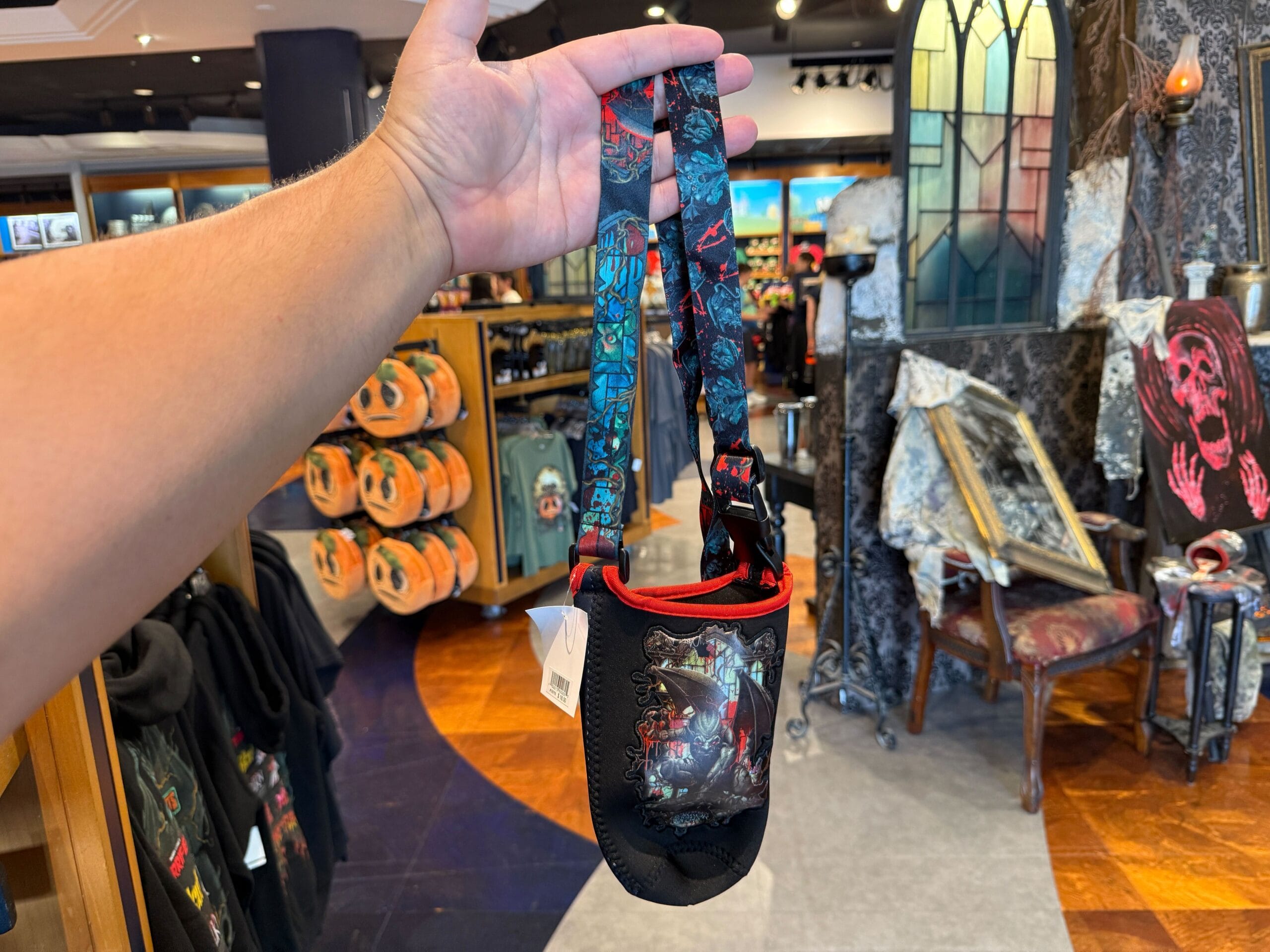 A hand holds a small black HHN merch pouch with a colorful strap inside the Universal Orlando Resort store.
