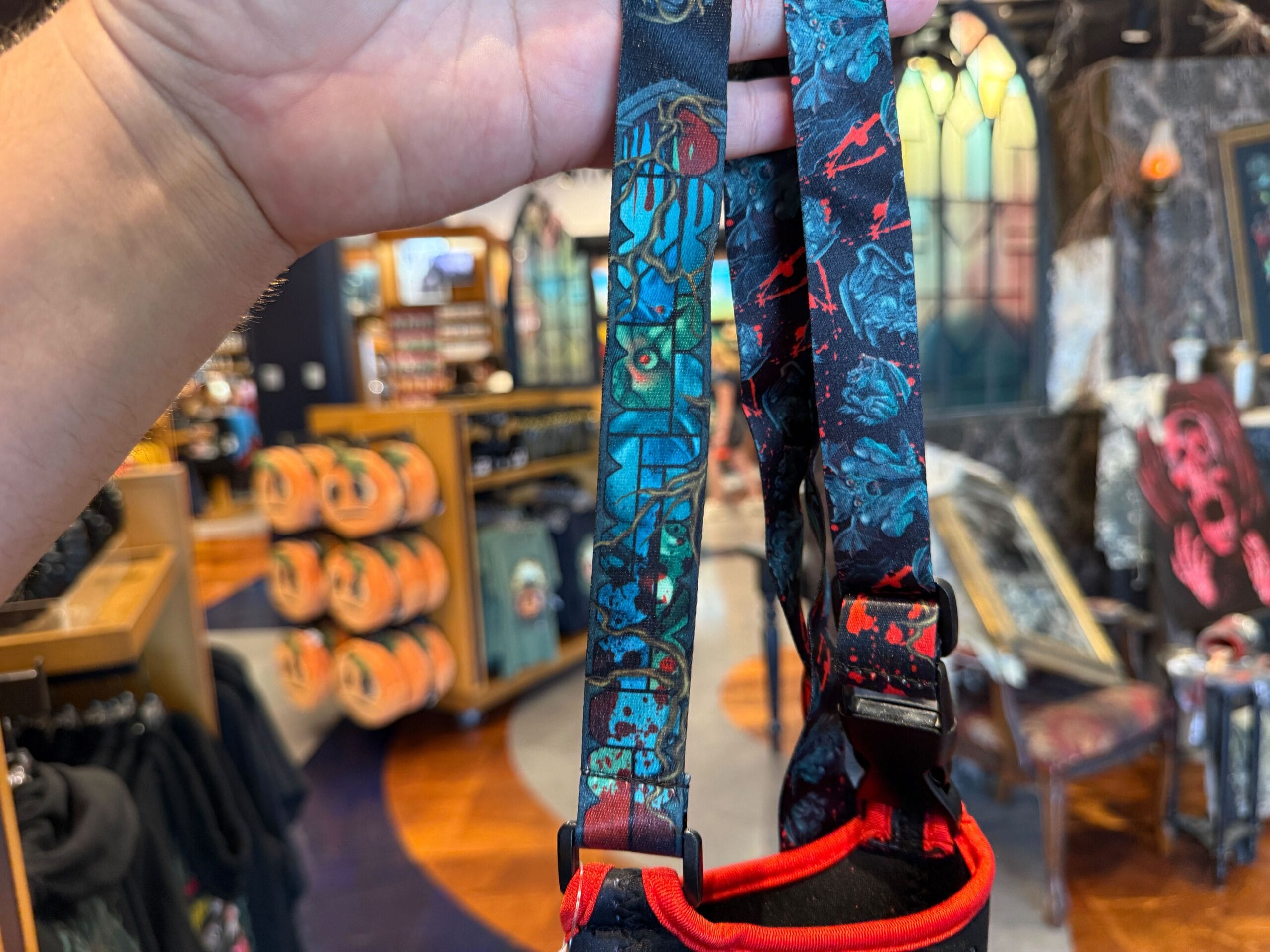 Close-up of a hand holding Halloween Horror Nights 2025 Merchandise lanyard in a store with festive decor and pumpkins.
