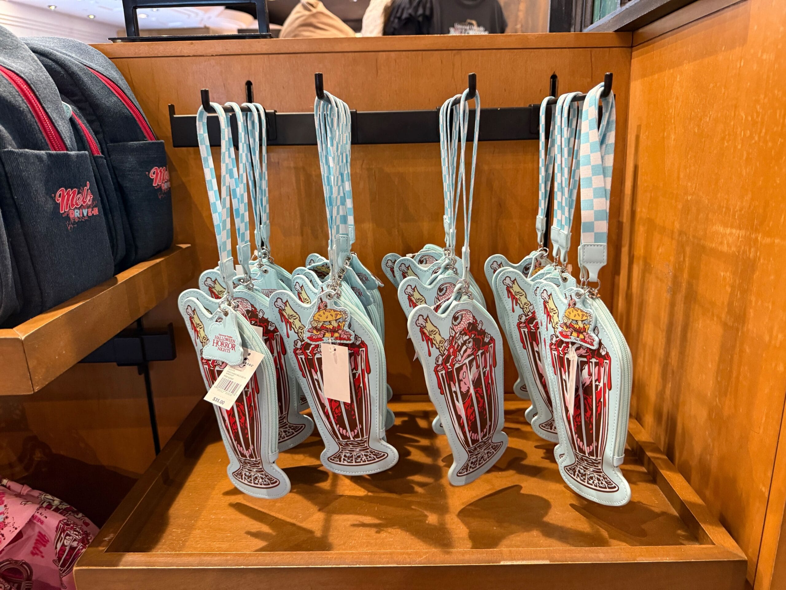 Several milkshake-shaped bag charms with blue checkered straps hang on display in a wooden store fixture.