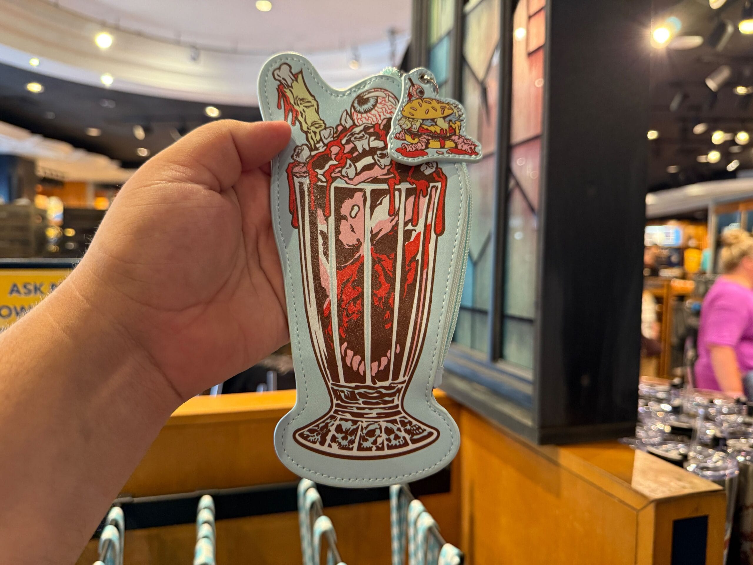 Hand holding a milkshake-shaped pouch featuring burger, fries, and popcorn toppings in a store setting.