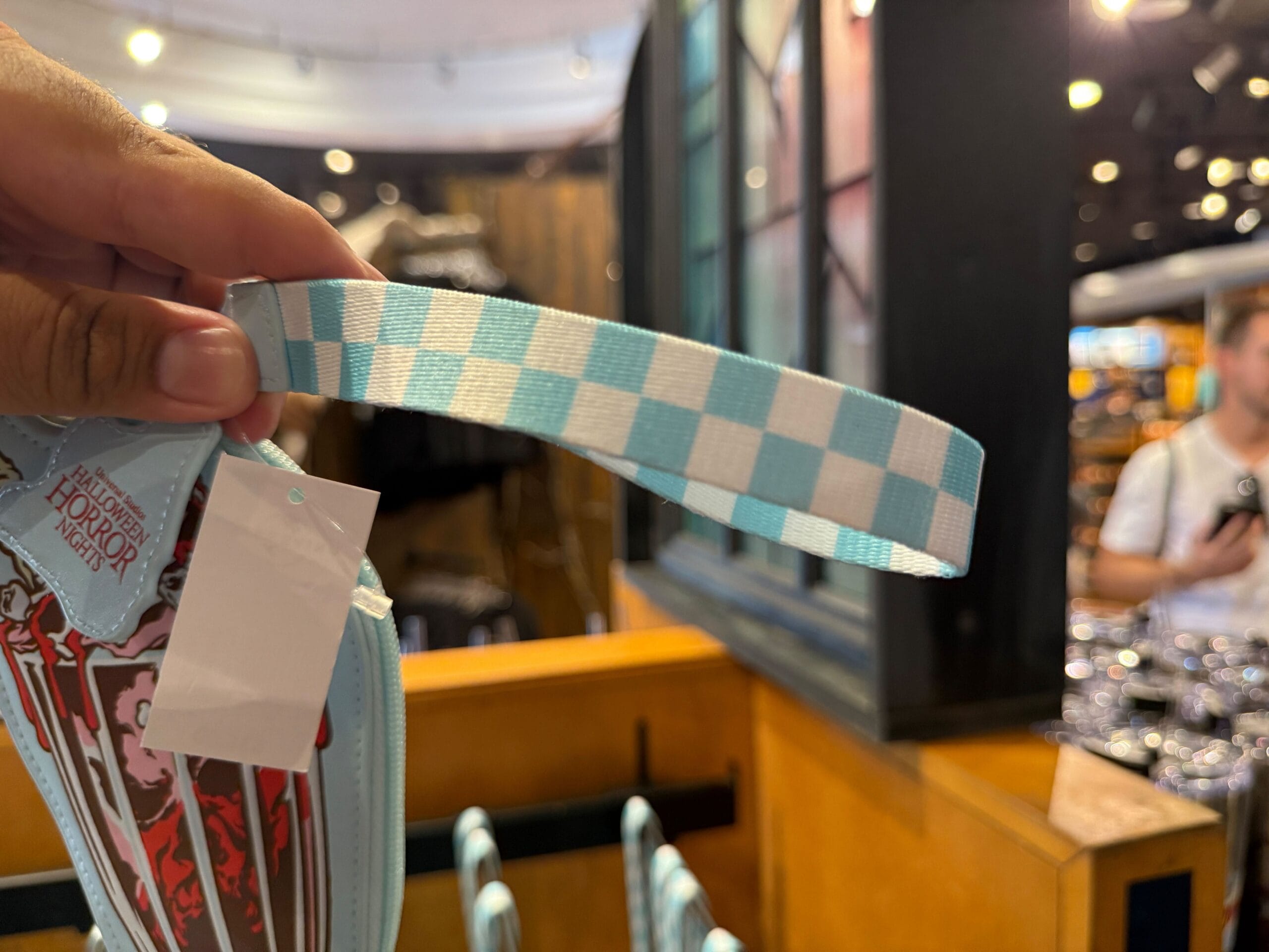 A hand holds a blue and white checkered strap attached to a bag inside a store.