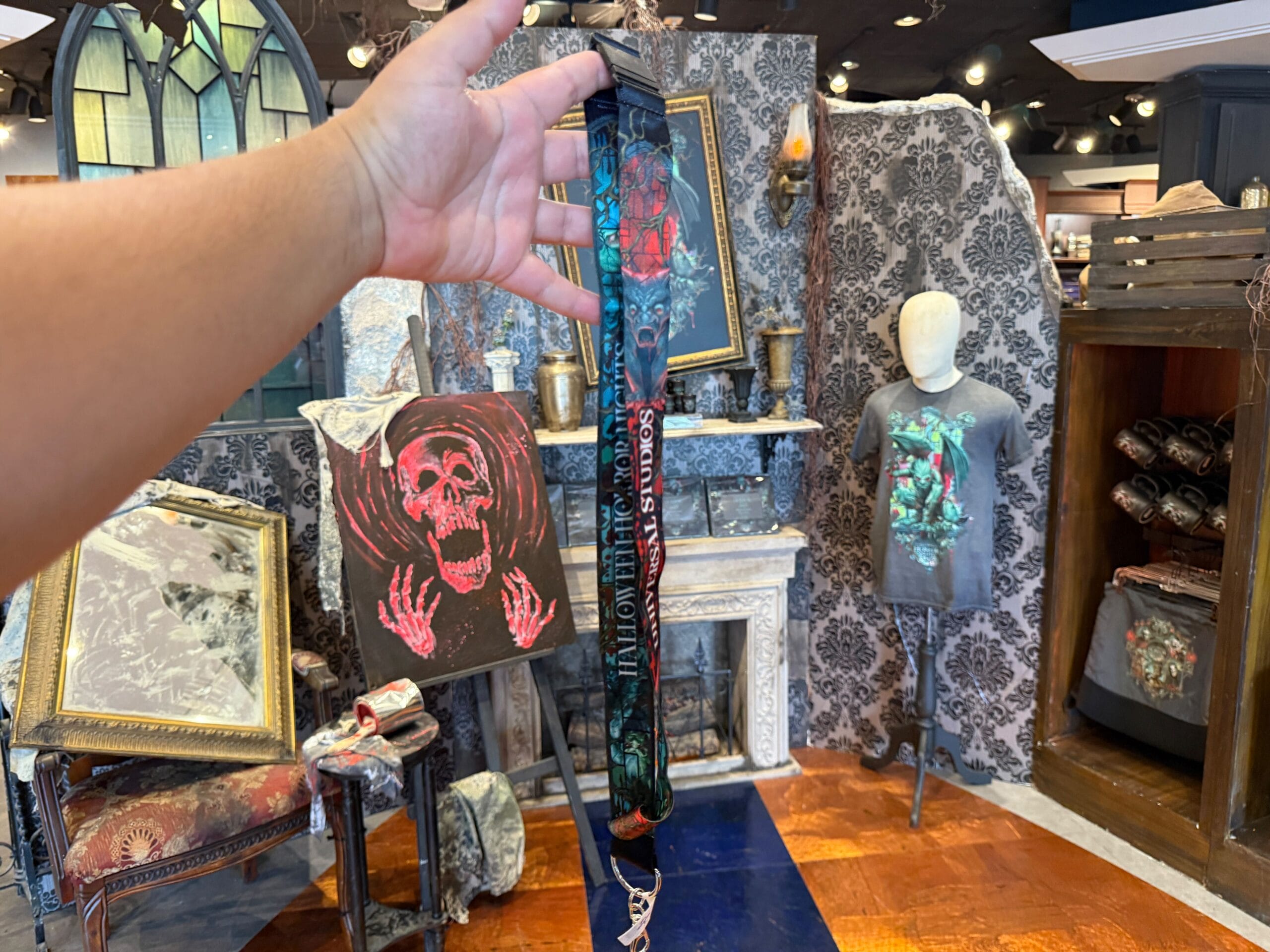A hand holds HHN merch in front of spooky decor and Universal Orlando Resort store displays.