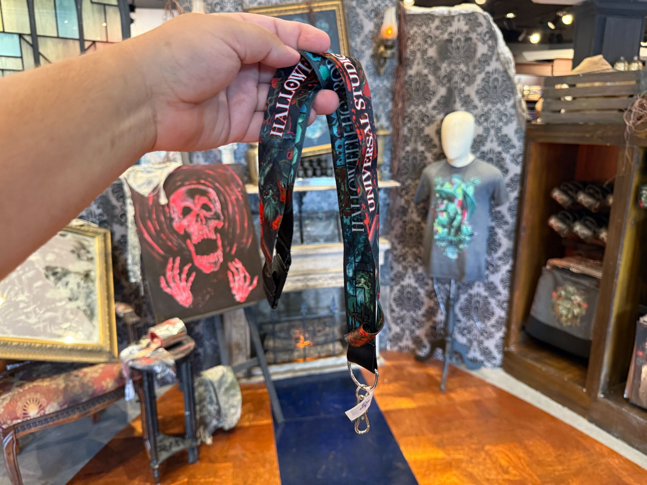 A hand holds a Halloween lanyard in a store filled with HHN merch and spooky decorations at Universal Orlando Resort.