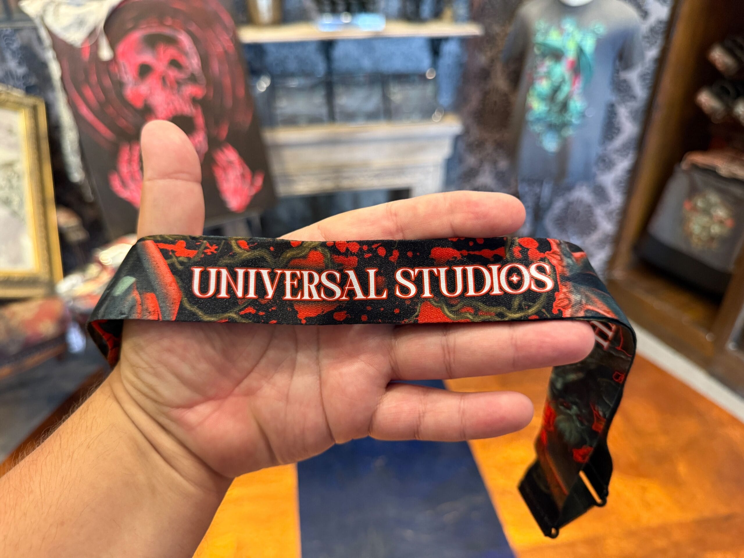 A hand holds a black and red Halloween Horror Nights 2025 lanyard inside a Universal Orlando Resort store.