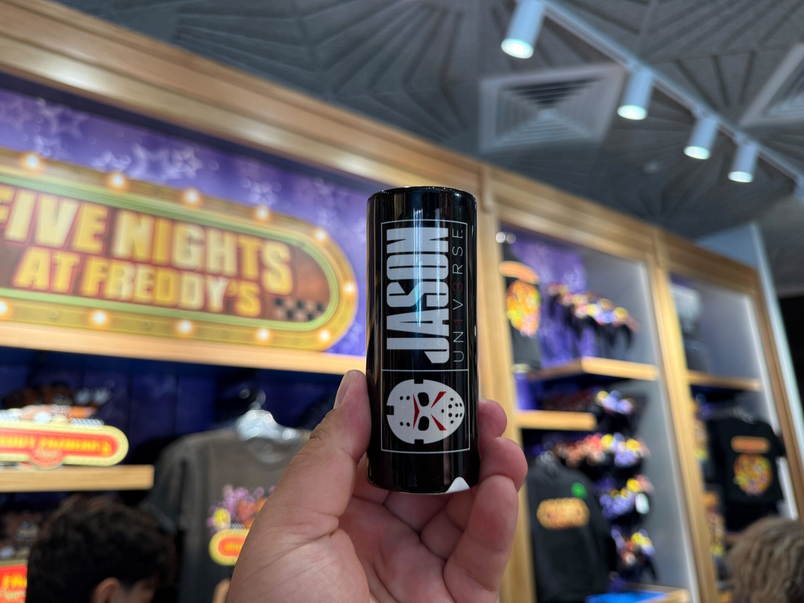 A hand holds a JASON UNIVERSE can before Five Nights at Freddy's and HHN Merch at Universal Orlando Resort.