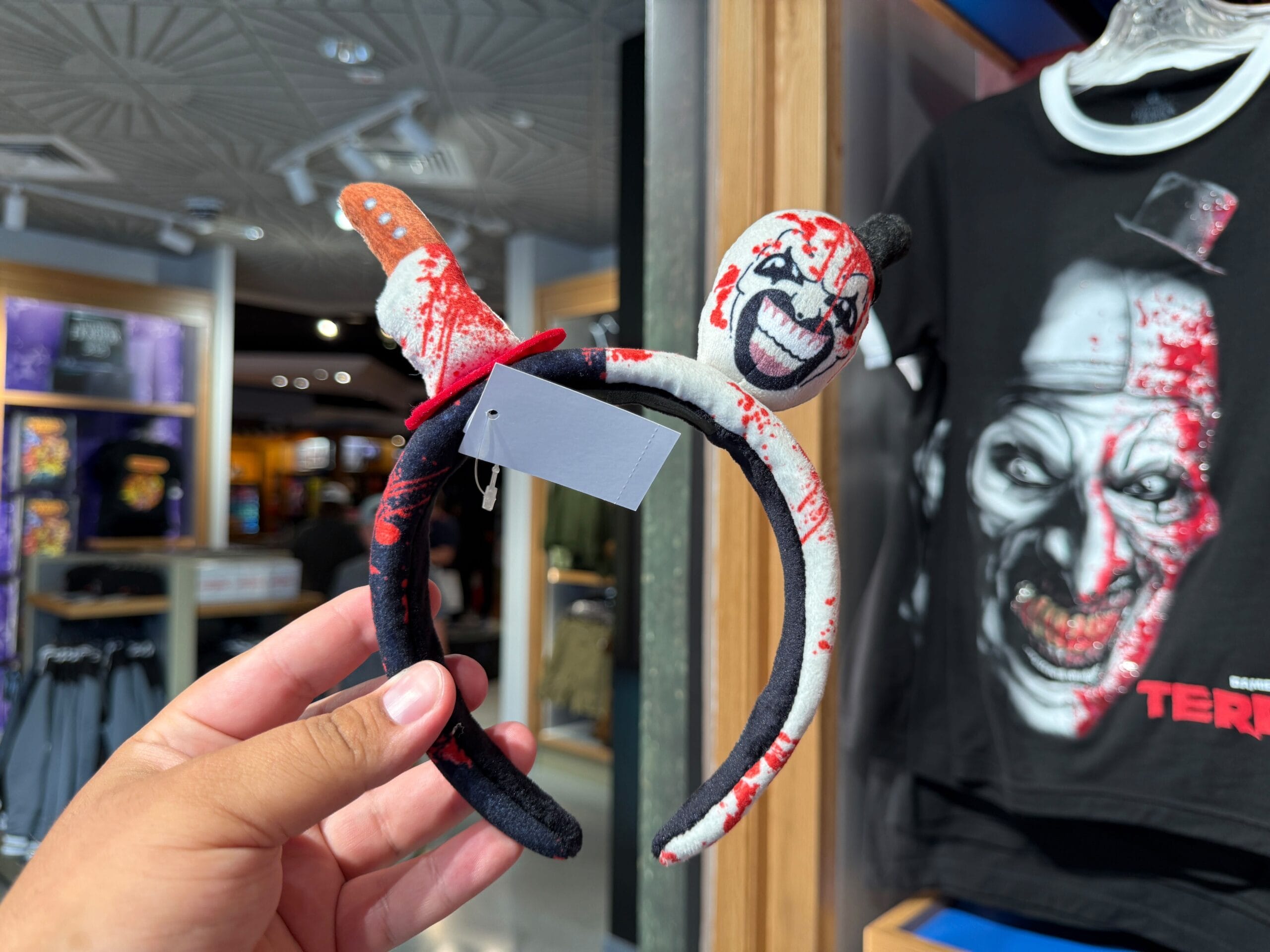 A hand holds a blood-splattered clown headband and toy knife—spooky HHN Merch at Universal Orlando Resort.