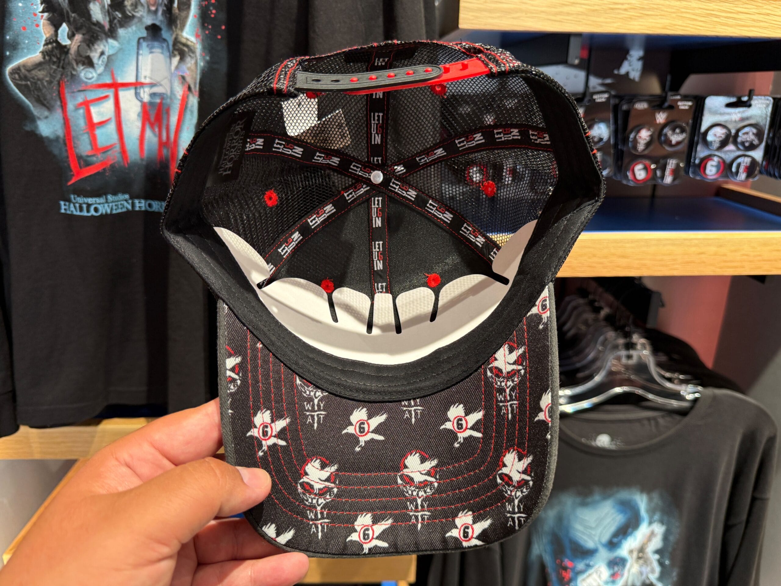 Hand holds a black cap with Halloween Horror Nights 2025 graphics, surrounded by HHN merch at Universal Orlando Resort.
