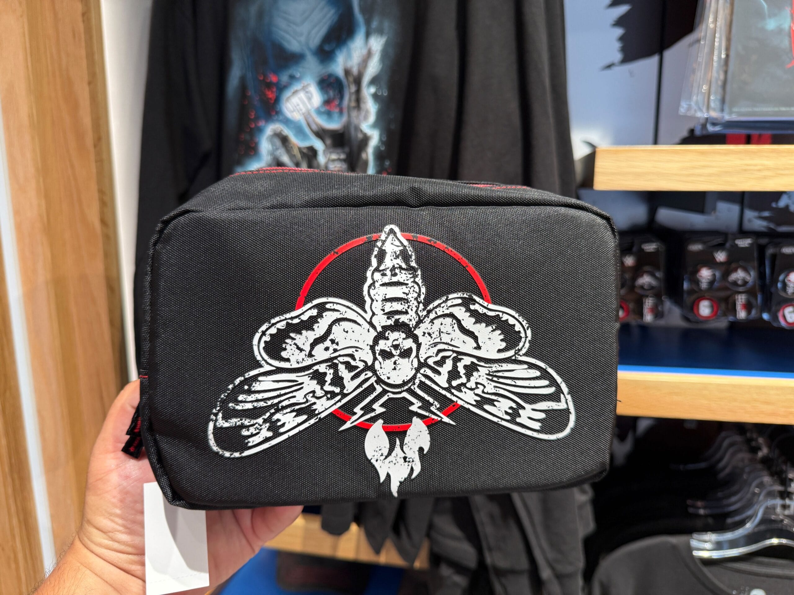 A hand holds a black pouch with a white moth and red accent, featured as HHN Merch at Universal Orlando Resort.