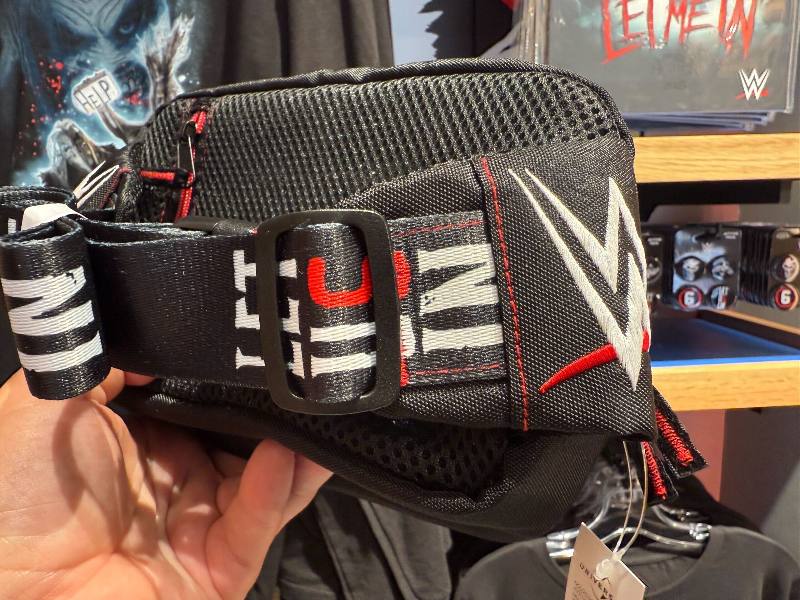 A hand holds a black WWE fanny pack with bold text, spotted at Universal Orlando Resort.