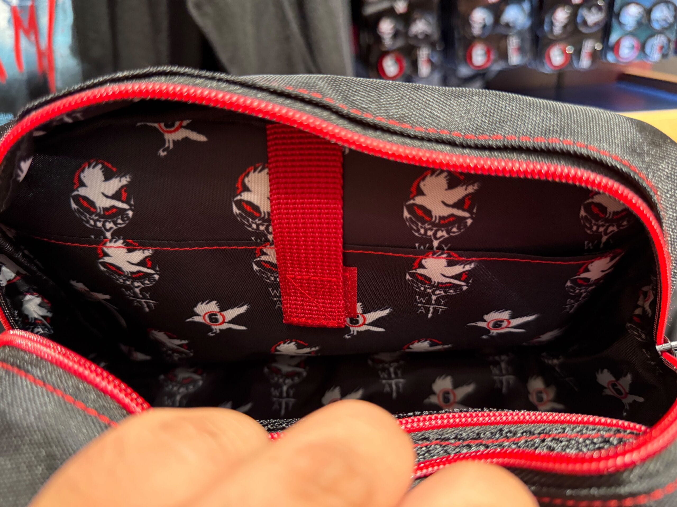 A hand opens a black and red bag, revealing HHN merch with stylized skull and bird patterns from Universal Orlando Resort.