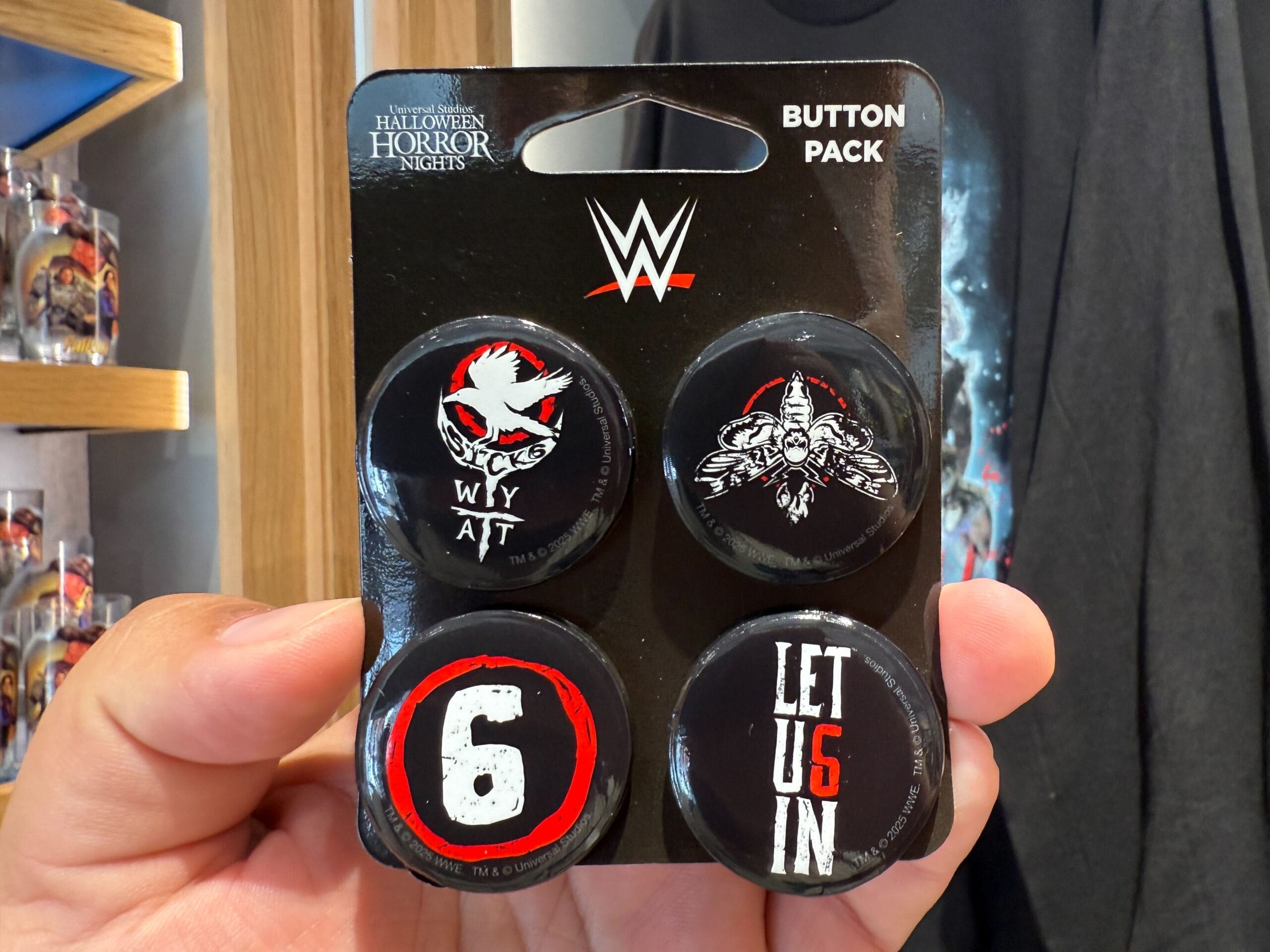 A hand holds a WWE button pack with four black pins—perfect for HHN Merch collectors at Universal Orlando Resort.