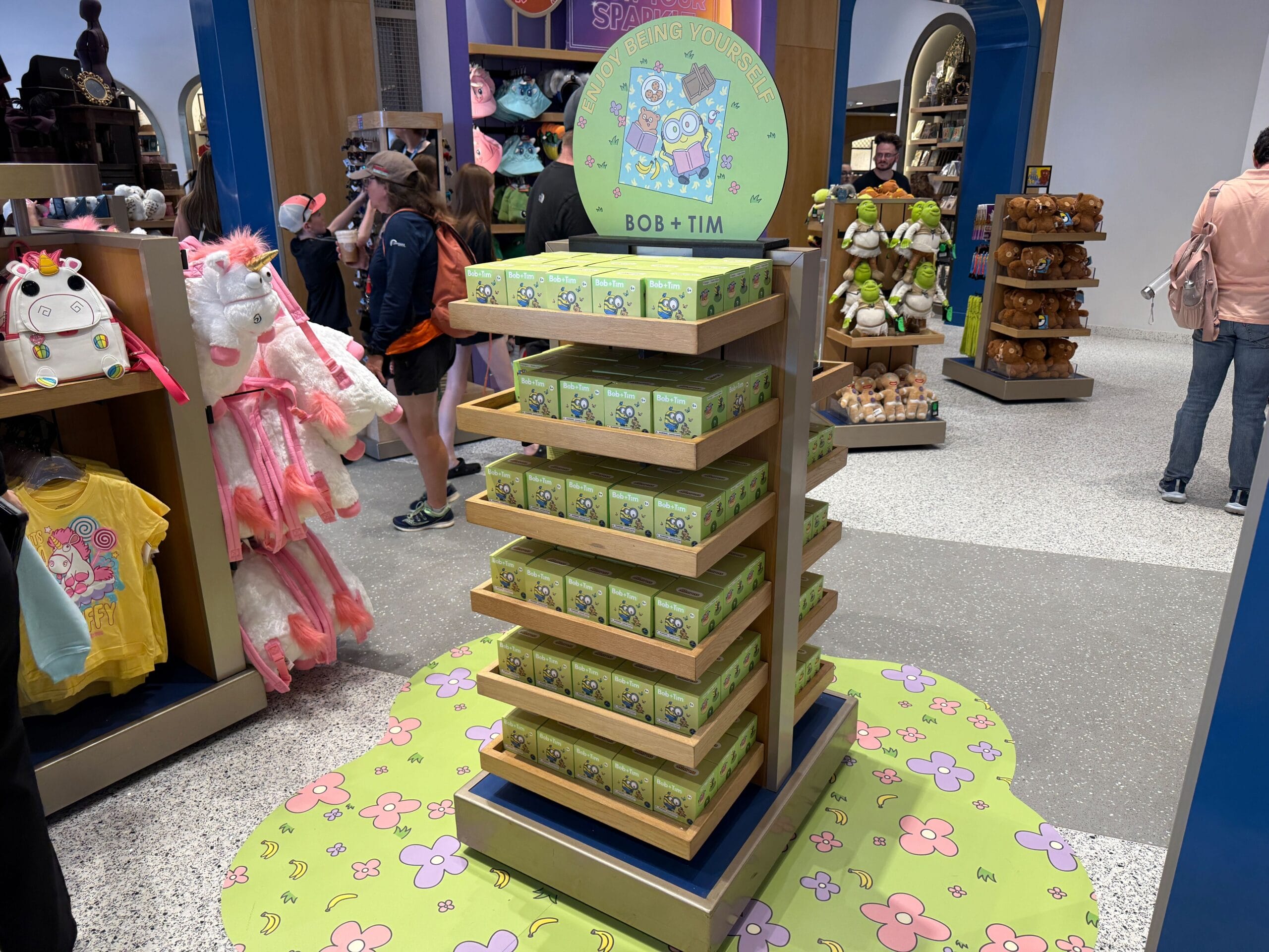 A display of stacked Bob & Tim mystery figures in the Universal Studios Store, surrounded by shoppers and plush toys.