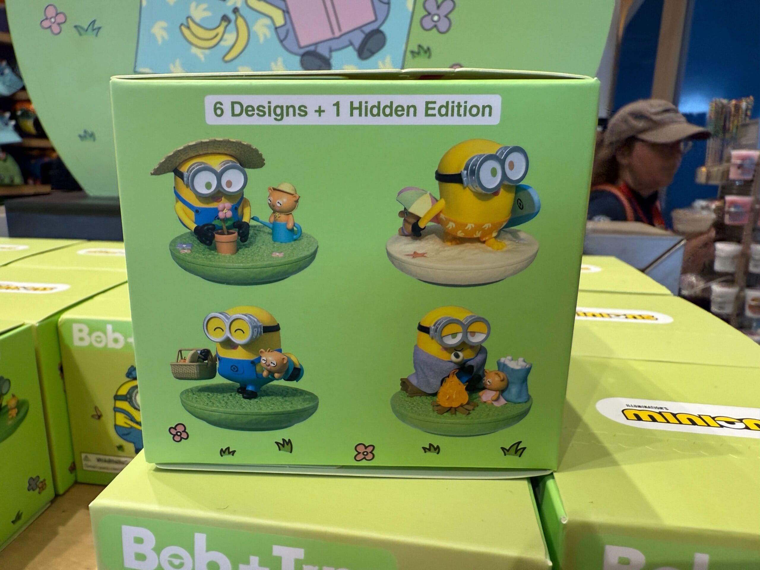 Box displaying four collectible Minion figures in different vacation scenes, labeled “6 Designs + 1 Hidden Edition.”