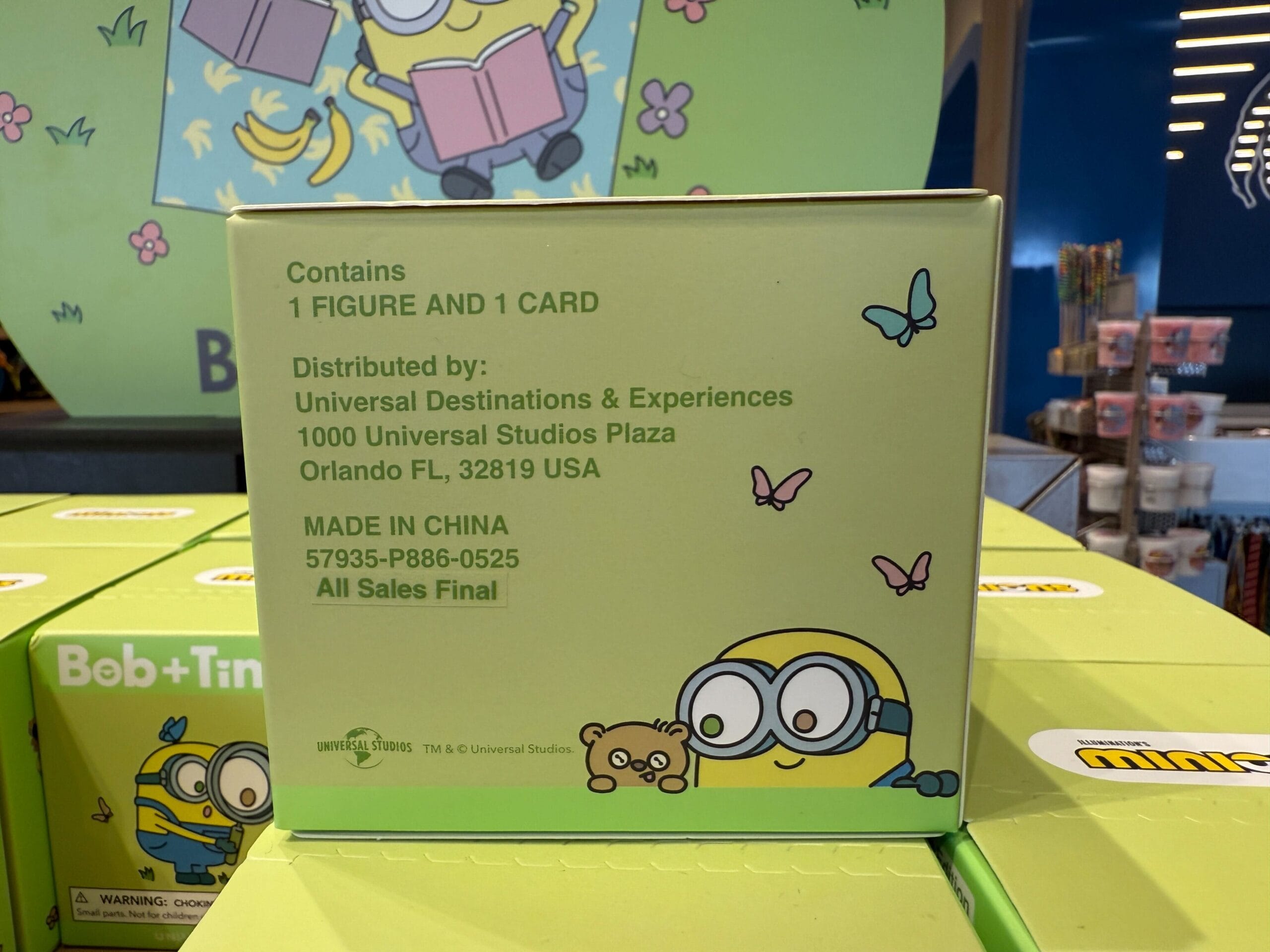 A green Minions toy box with text listing contents and distributor info, plus cartoon Minions and butterflies.