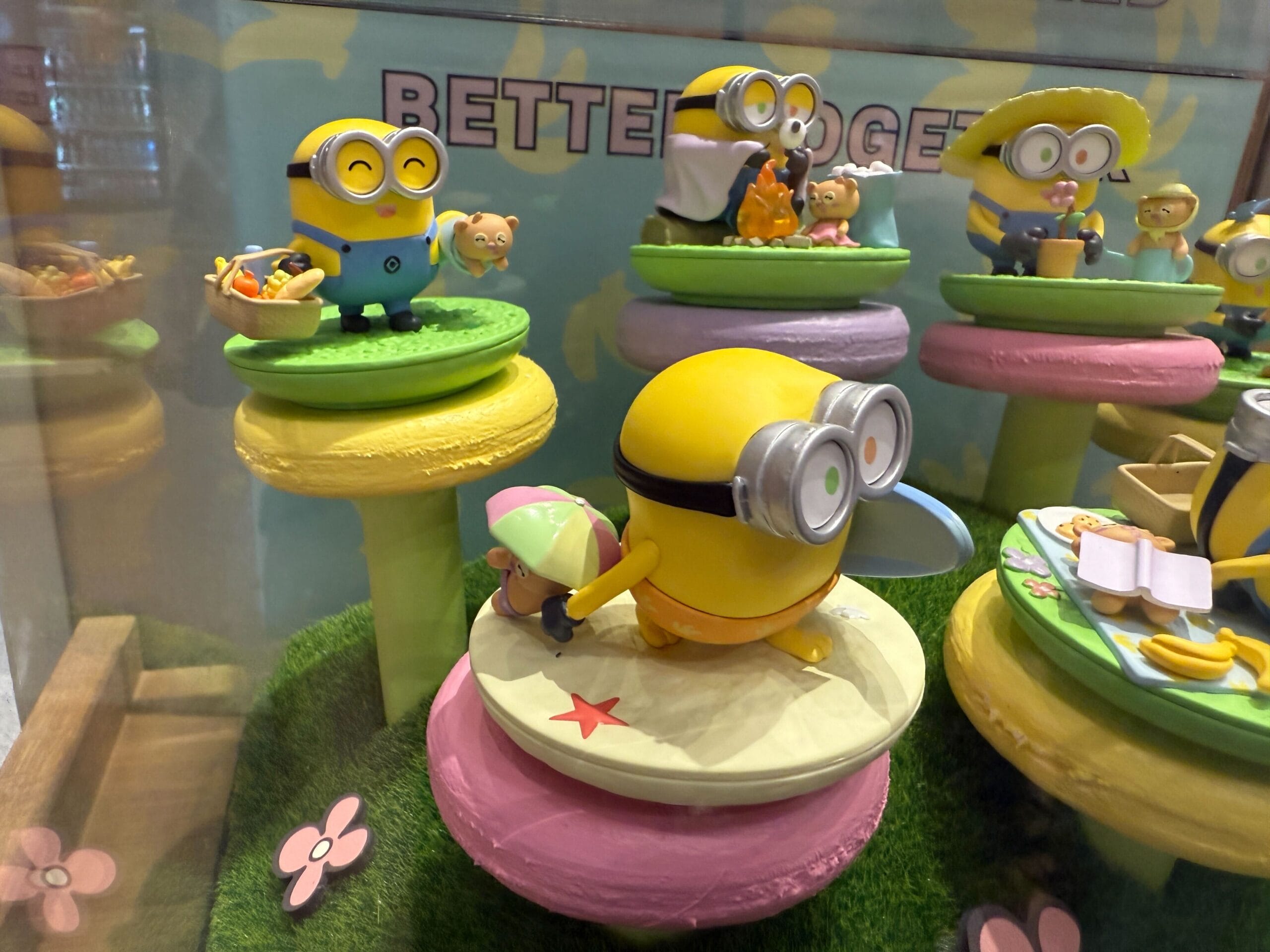 Toy Minions and animals are displayed on colorful platforms with grass and flowers in the background.