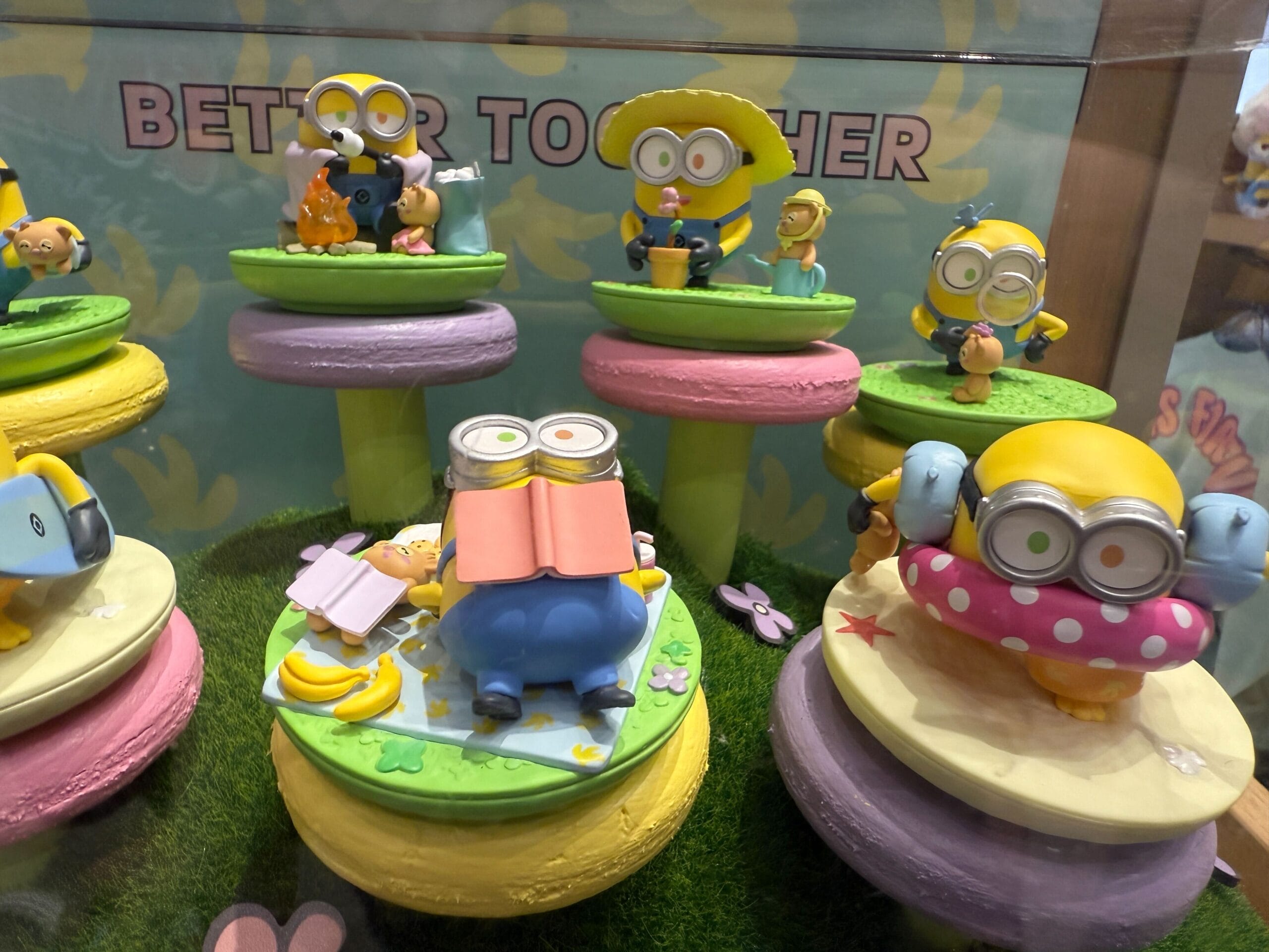 Colorful Minion figurines doing various activities, displayed on tiered platforms with a "BETTER TOGETHER" sign behind them.
