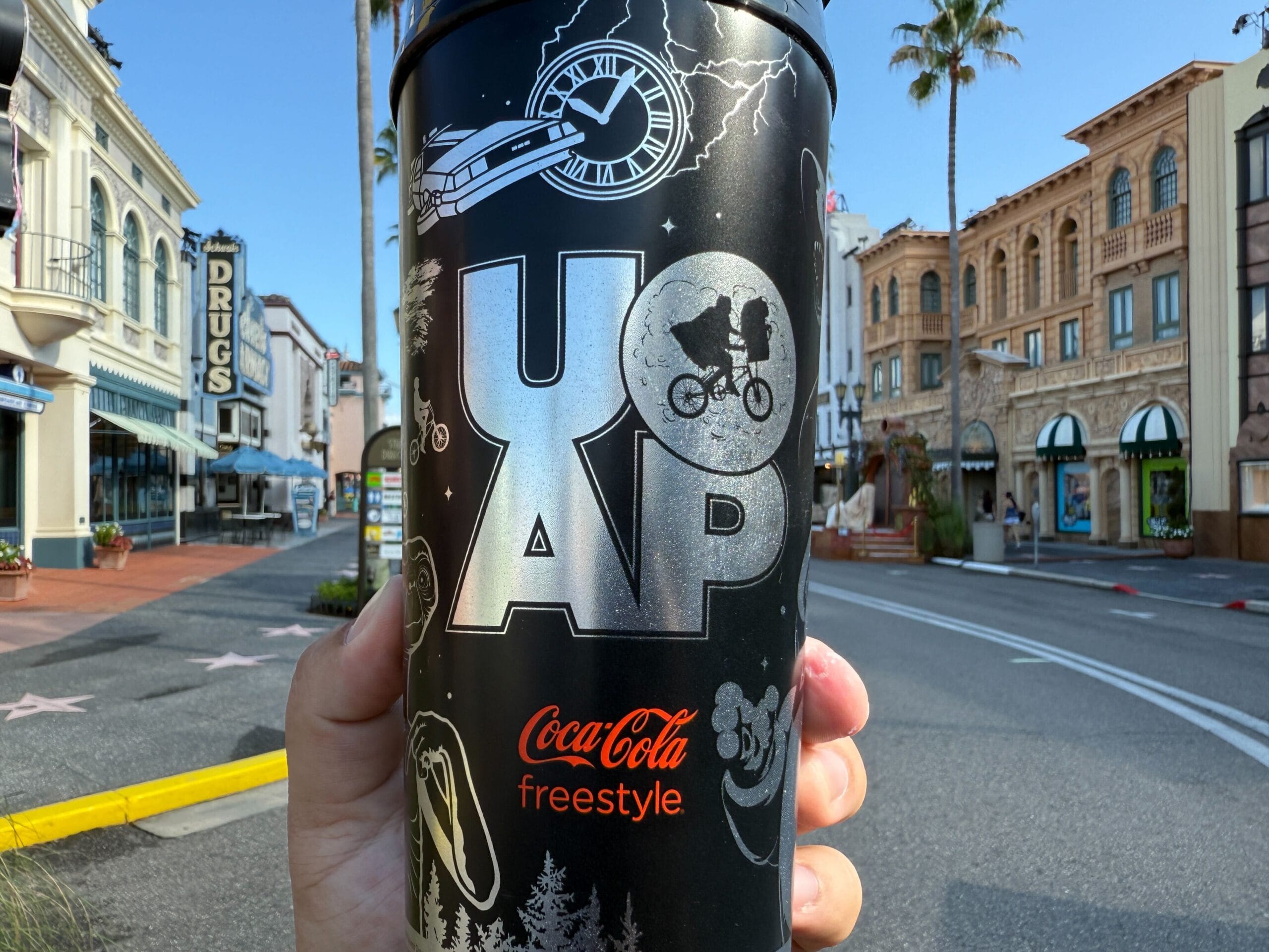 Hand holding a Coca-Cola Freestyle Cup with movie-themed stickers during UOAP Passholder Appreciation Days.