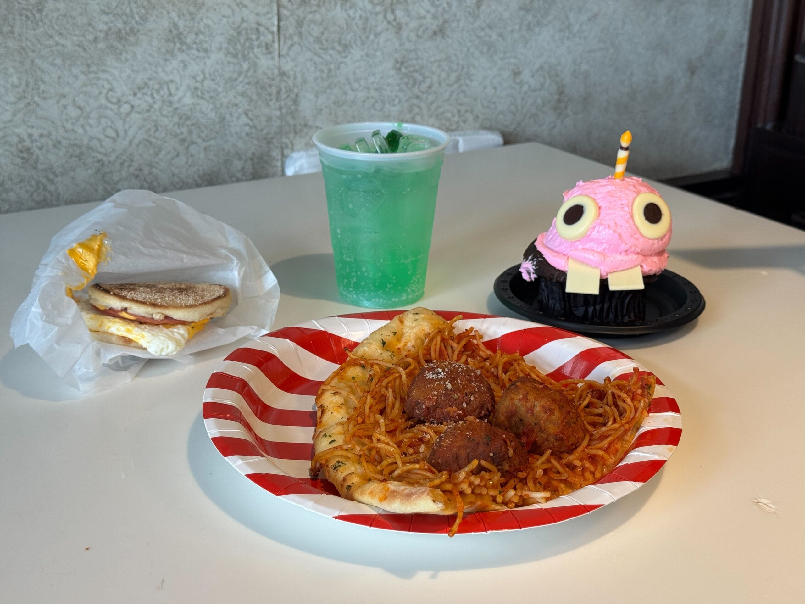 A table with a breakfast sandwich, spaghetti, green drink, and a Five Nights at Freddy's Pizza-themed cupcake.