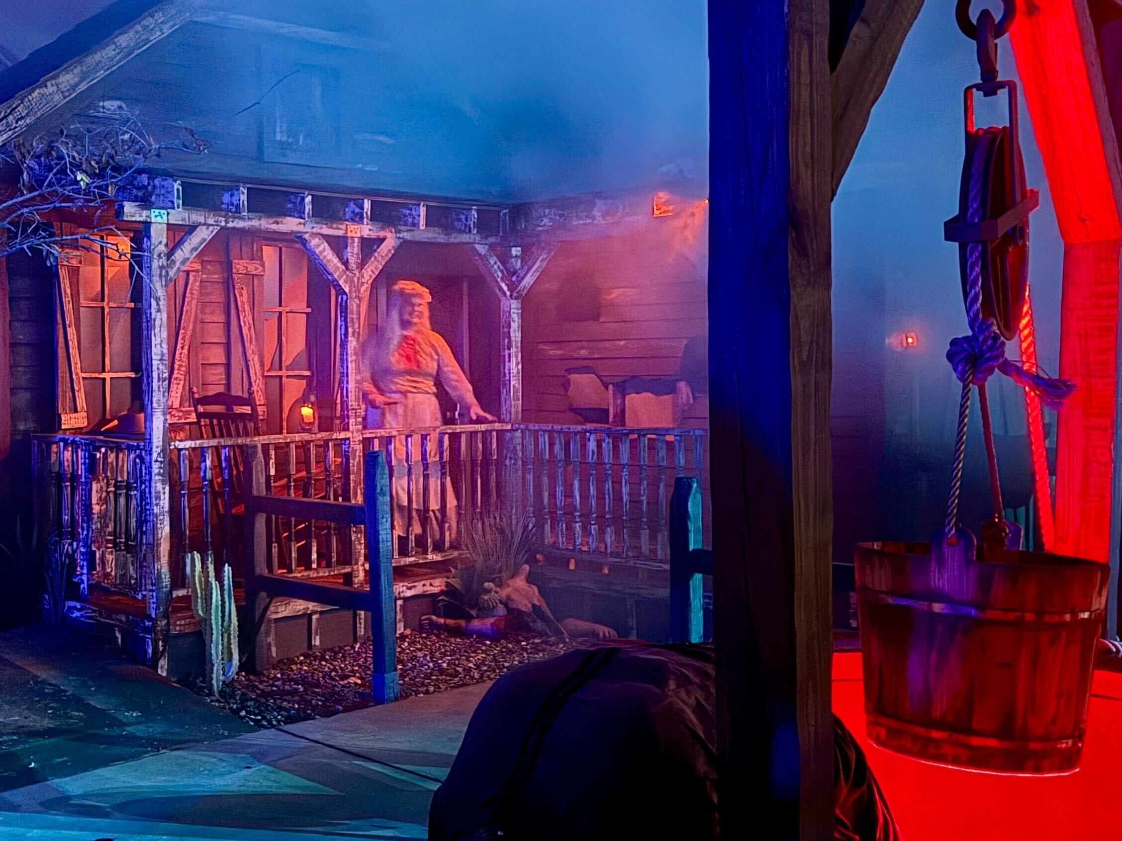 A person in costume stands on a foggy porch at night, lit eerily for HHN 2025, with a Demon Bounty Hunters vibe.