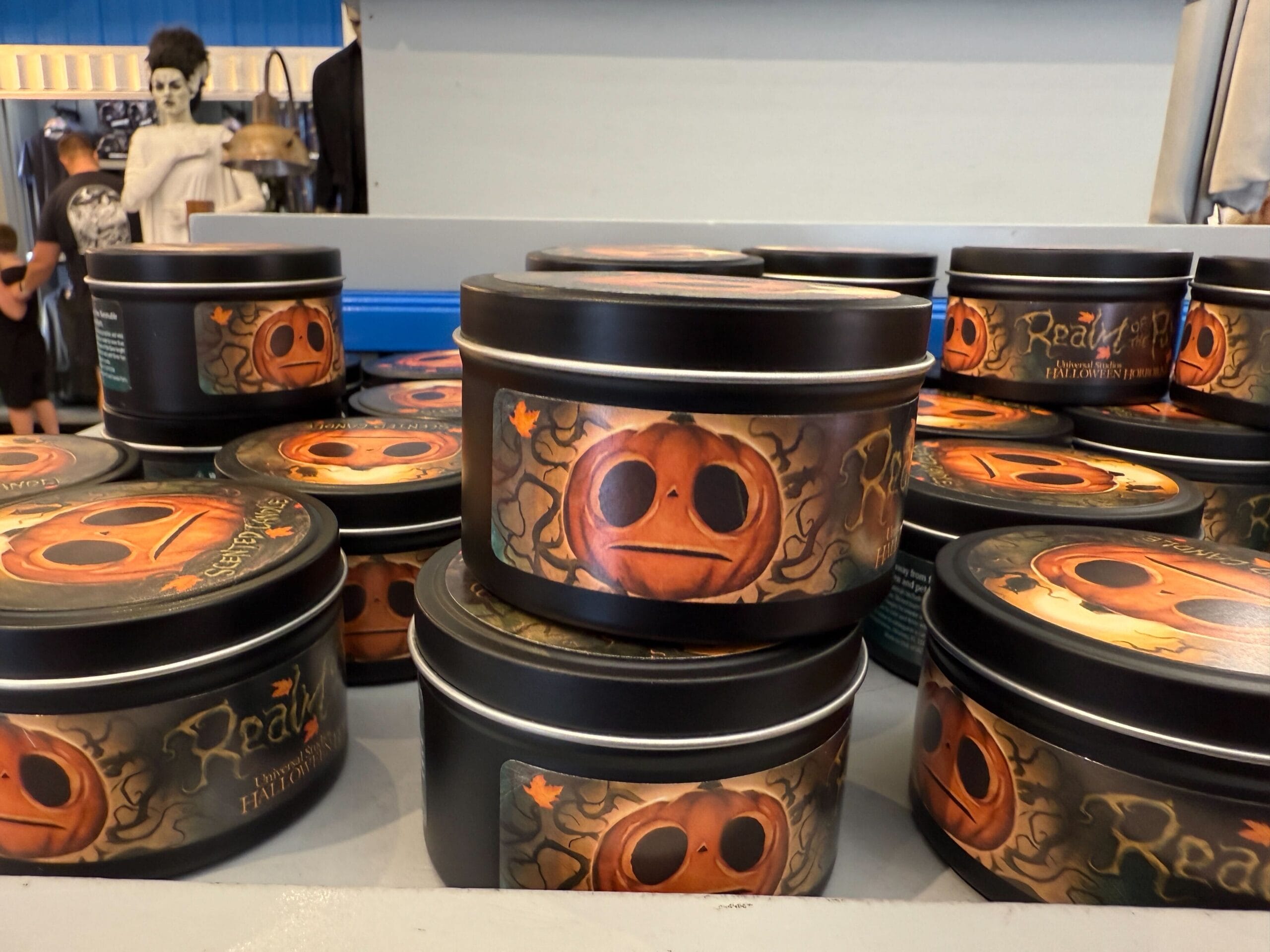 Stacked tins with pumpkin faces and autumn leaves; Lil Boo merch and Halloween decor visible on the store shelf.