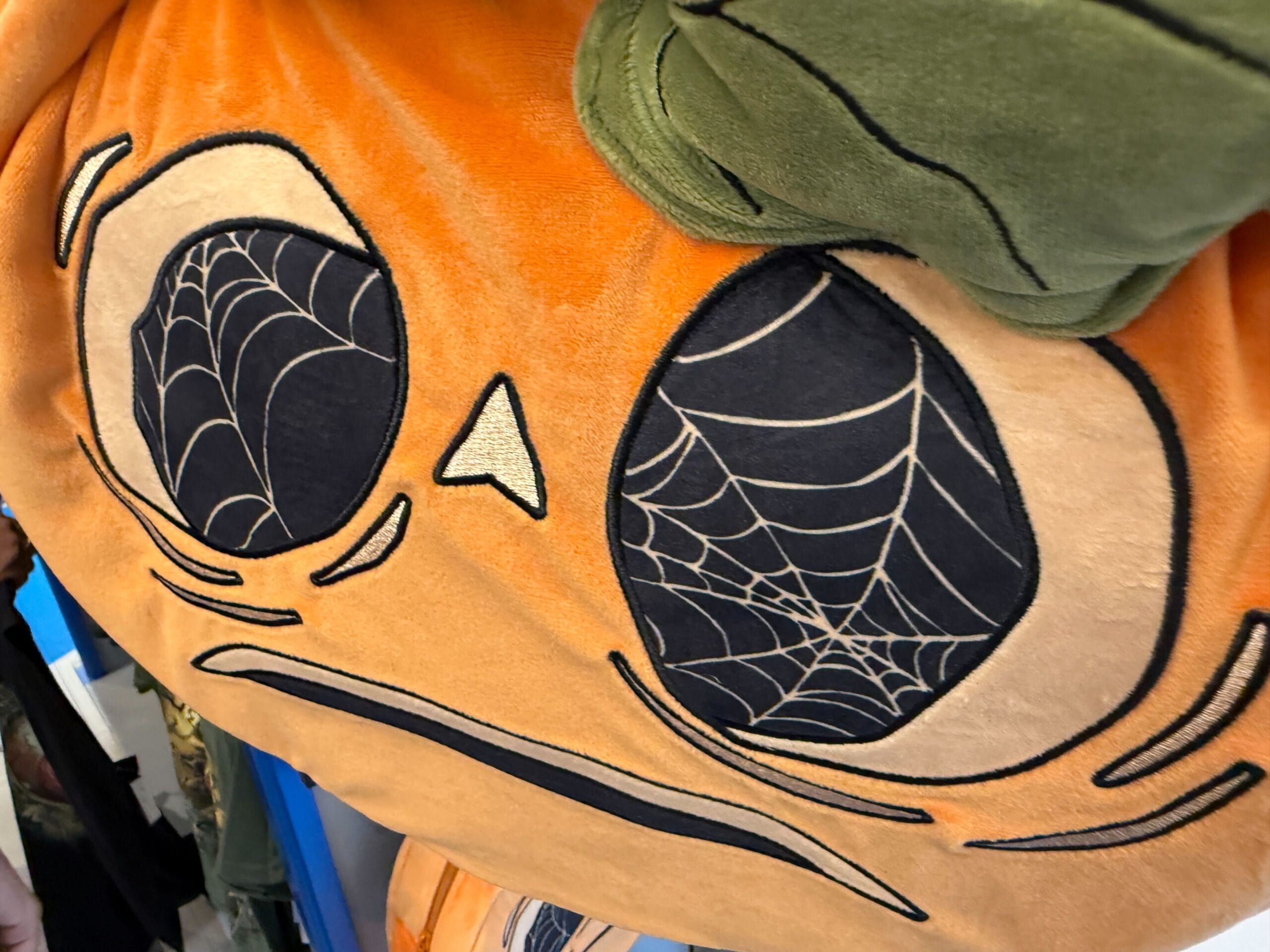 Close-up of Lil Boo Merchandise: plush pumpkin face with spiderweb eyes and a green stem on top.