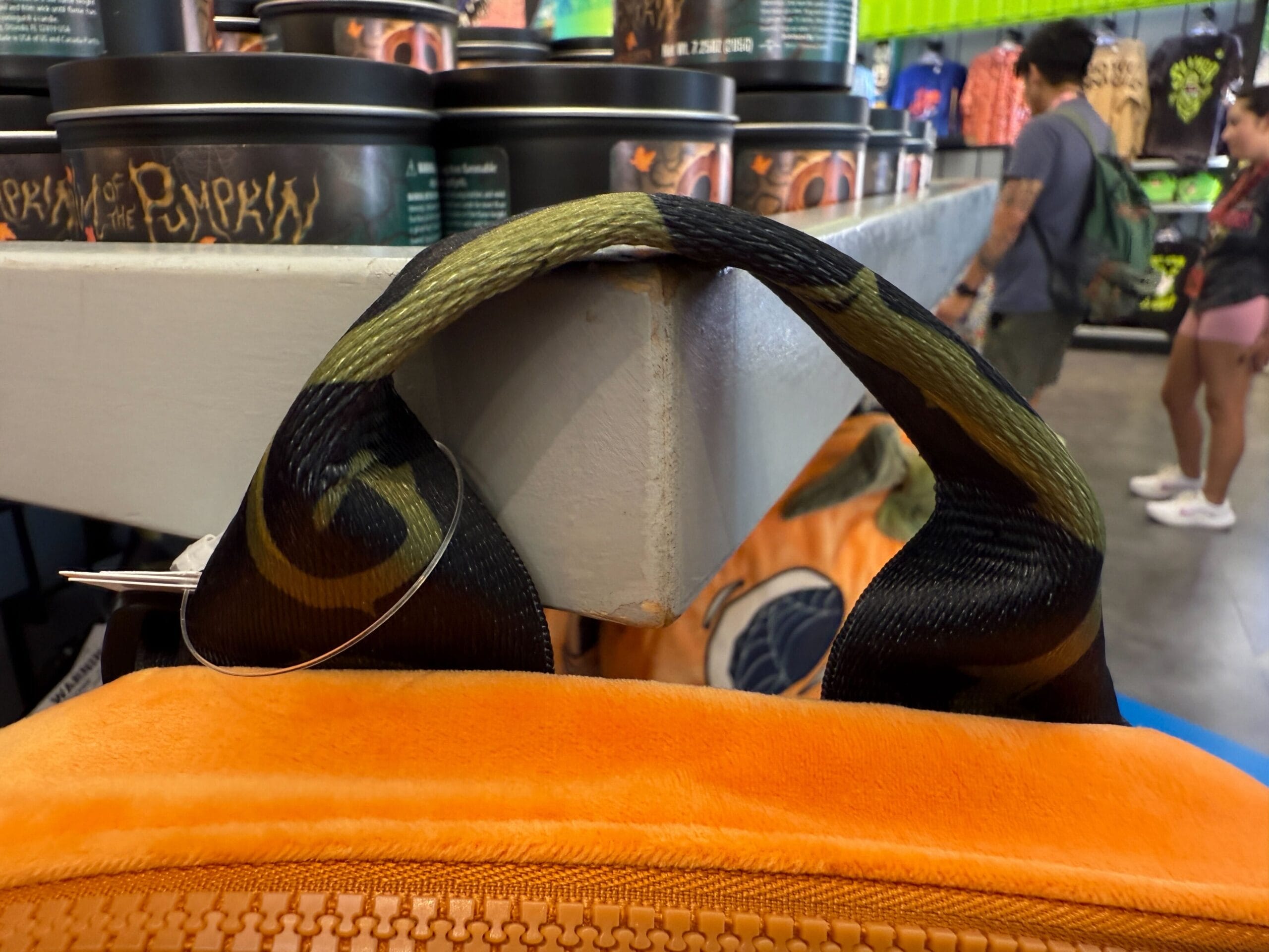 Close-up of a Lil Boo merch backpack handle caught on a store shelf, with people shopping in the background.