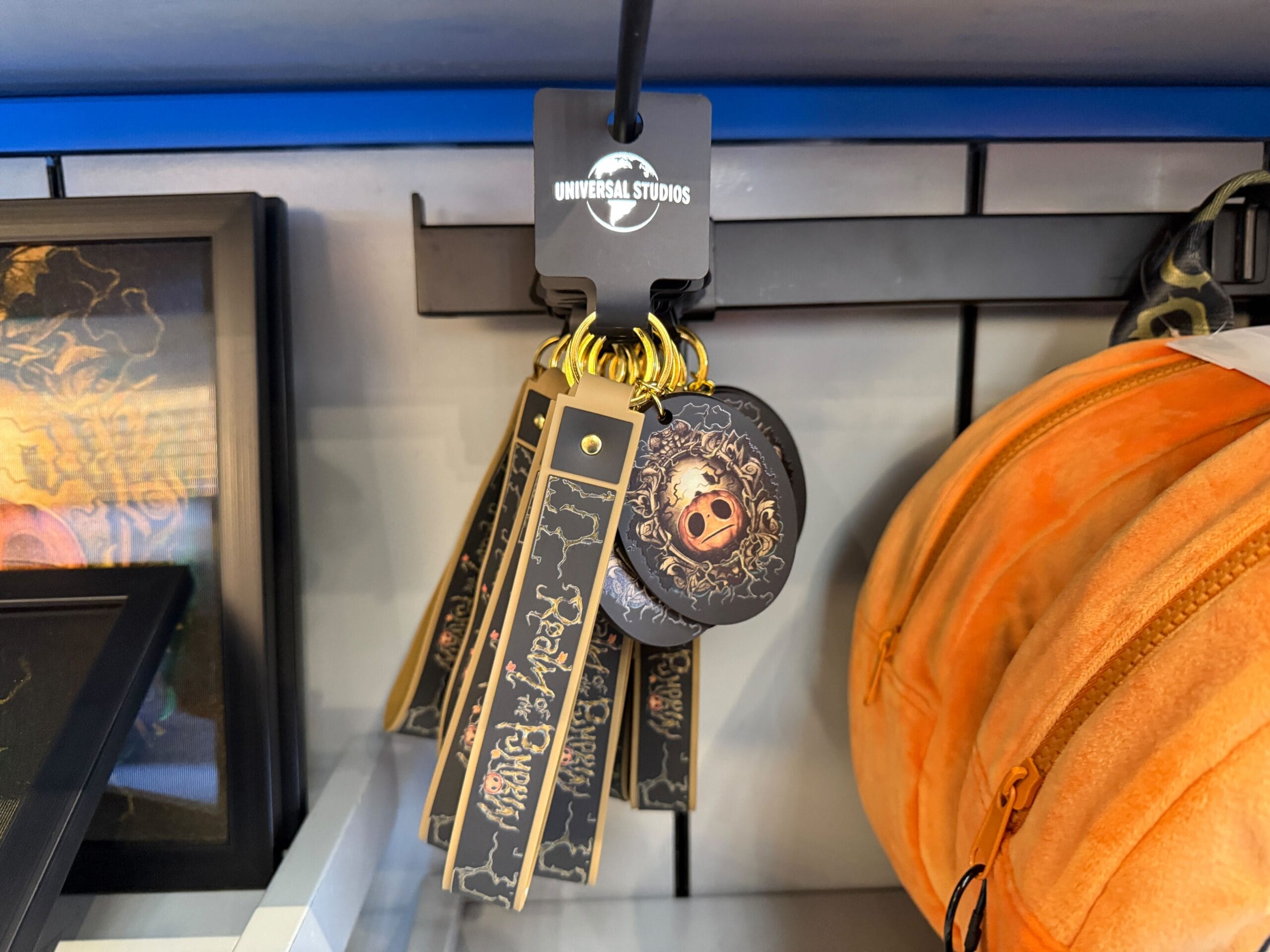 A set of Universal Studios keychains, including Lil Boo merch with dark designs and gold lettering, hangs on display.