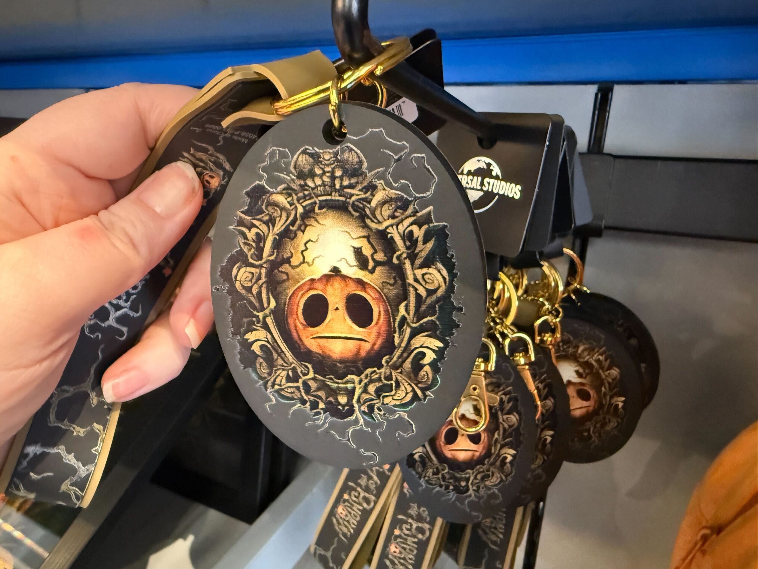 A hand holds a Universal Studios lanyard with a round Lil Boo Merchandise tag featuring a gold pig-like helmet design.