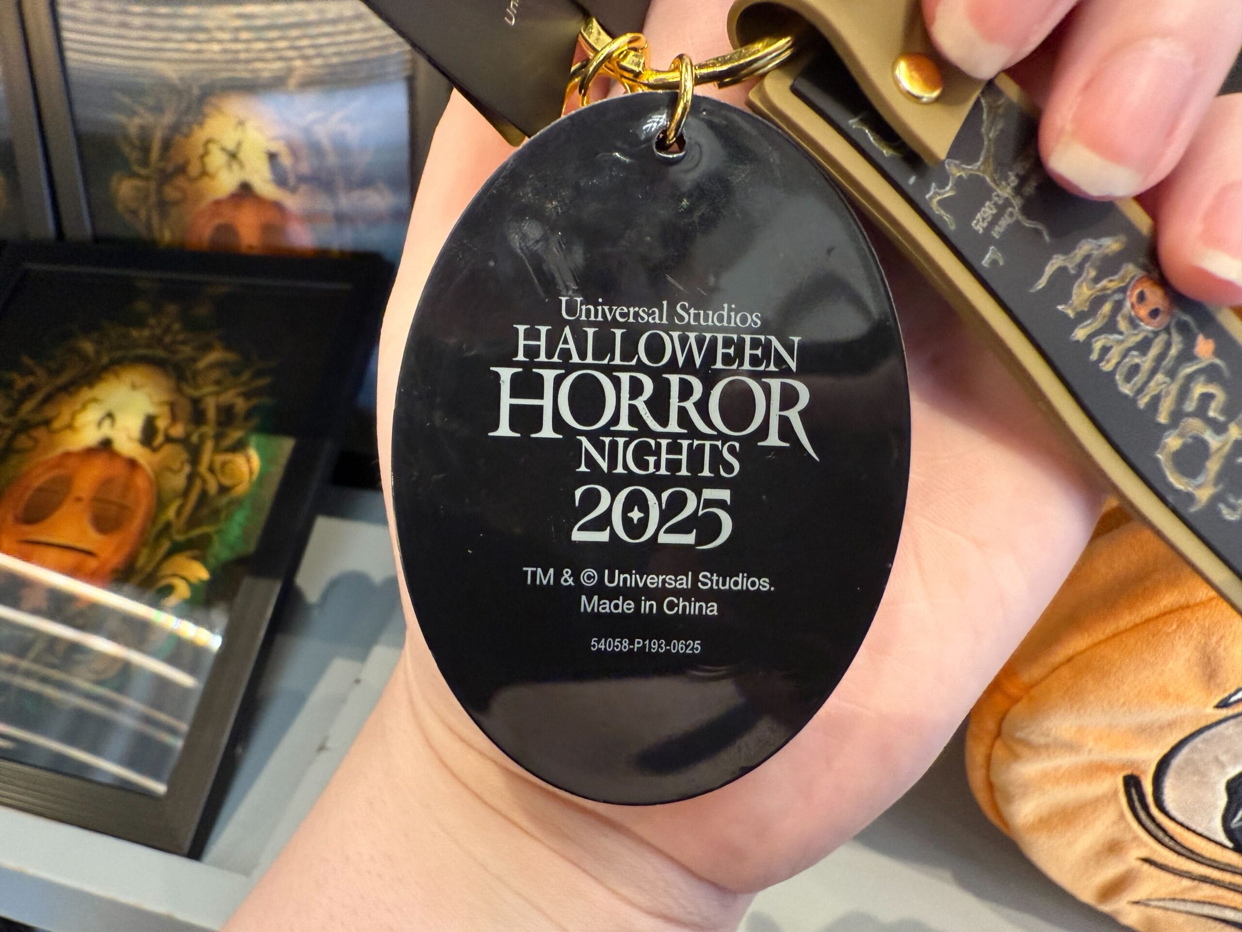 A hand holds a black "Halloween Horror Nights 2025" tag from Universal Studios Lil Boo Merchandise.