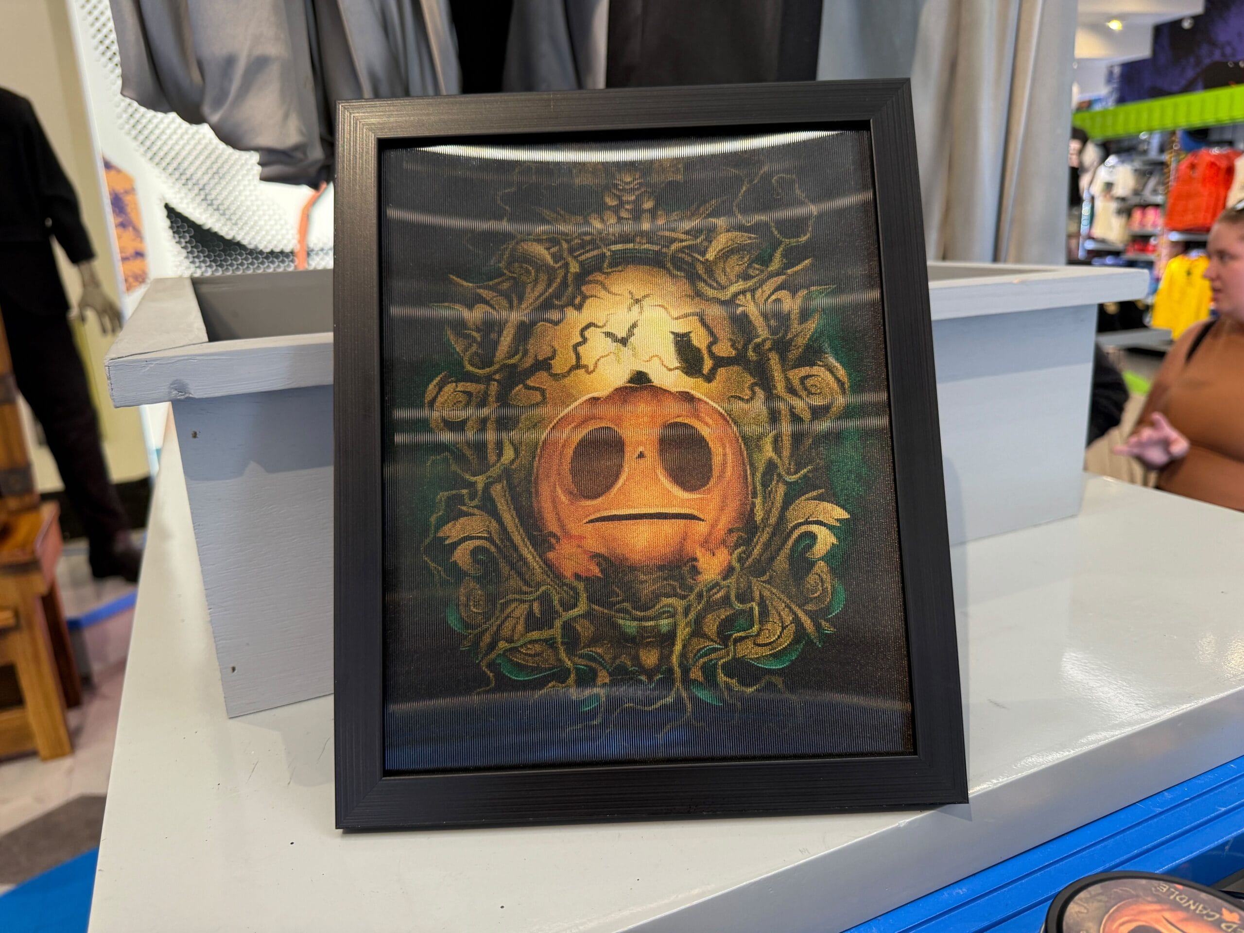 Framed Lil Boo Merchandise artwork of a stylized face with large eyes and ornate golden designs, displayed on a shelf.