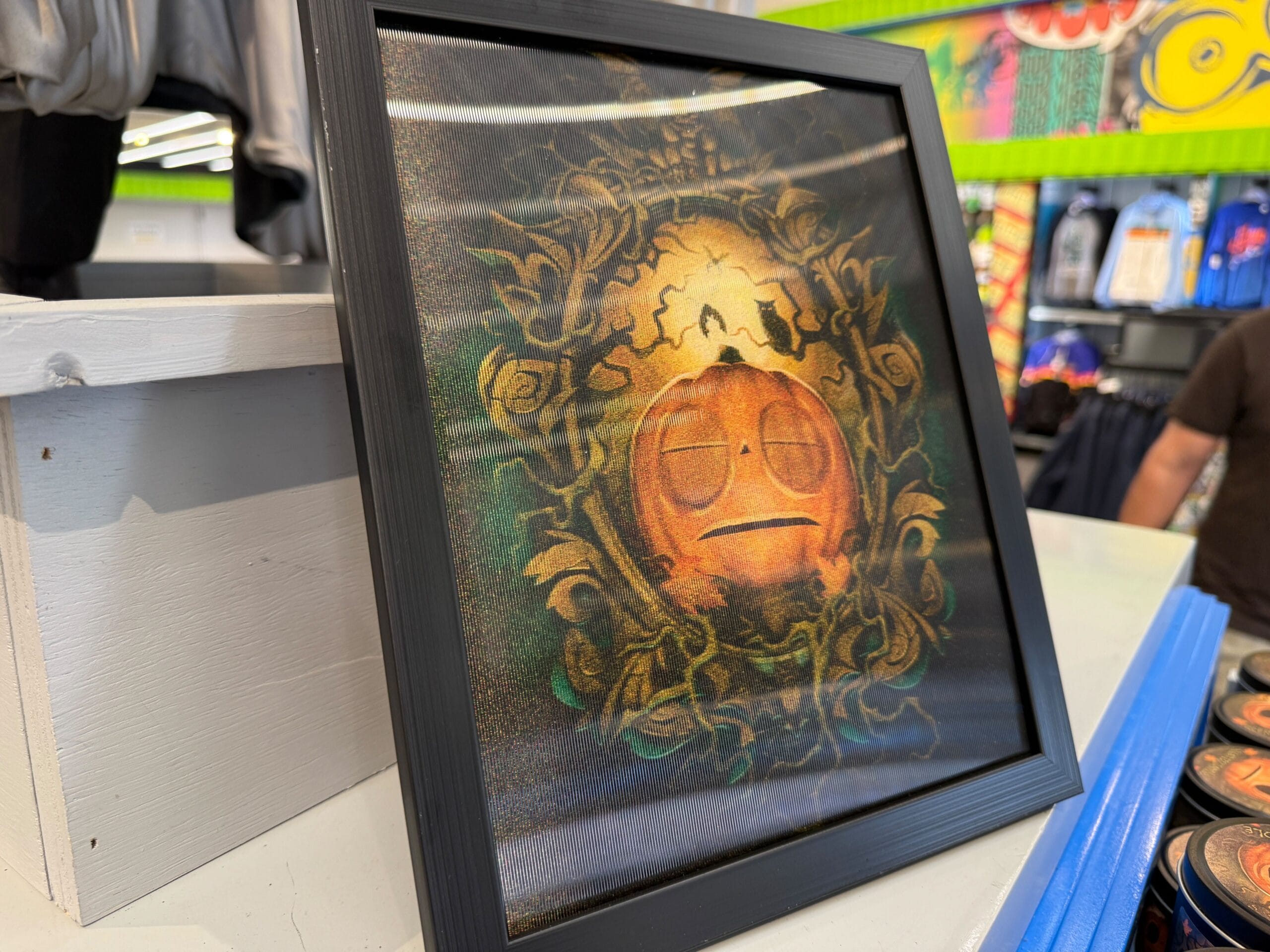 Framed Lil Boo Merchandise art of a pumpkin with a neutral face, ornate vines, and details on a store shelf.