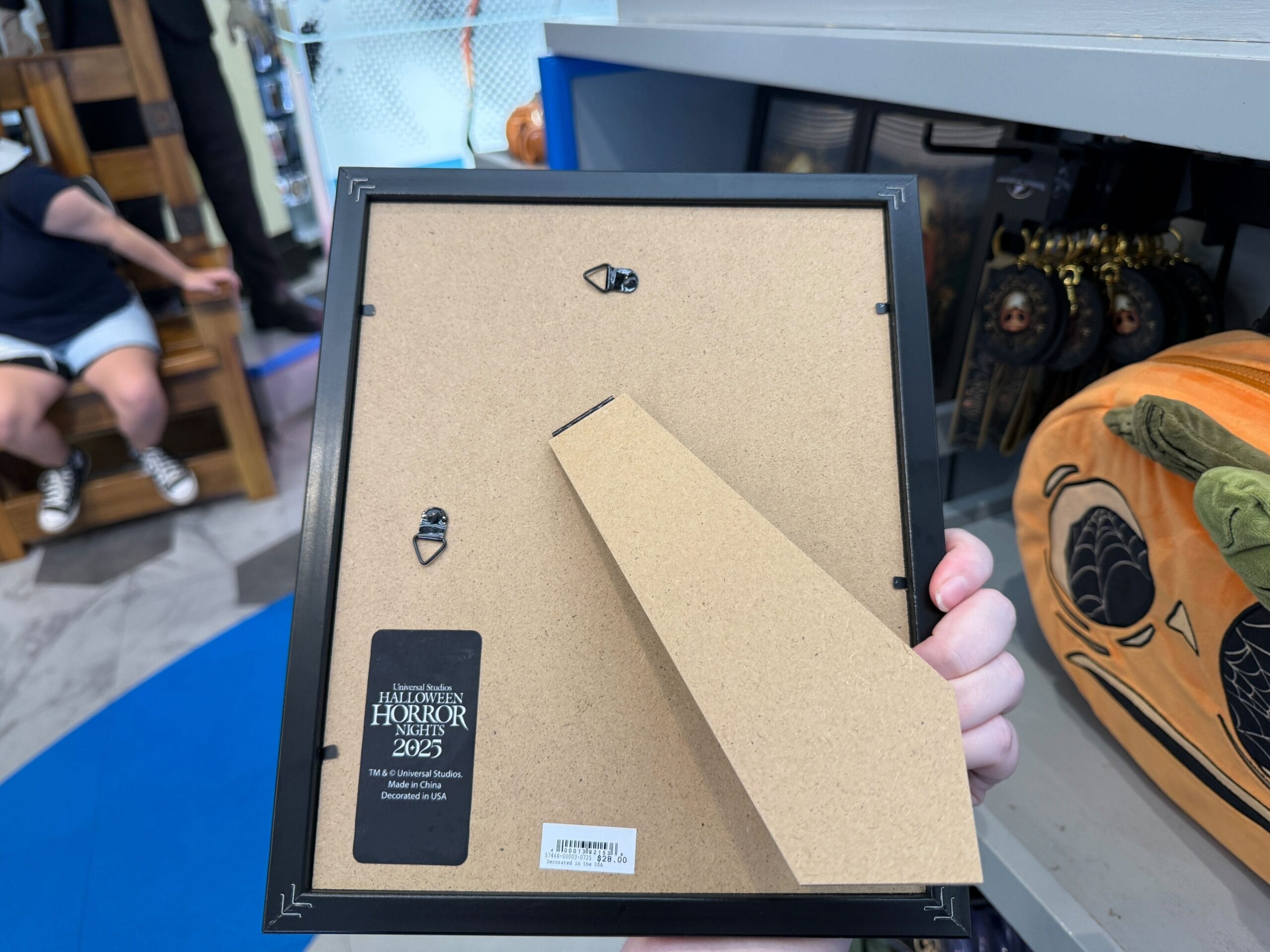 A hand holds a wooden photo frame in a store near Halloween-themed Lil Boo Merchandise.
